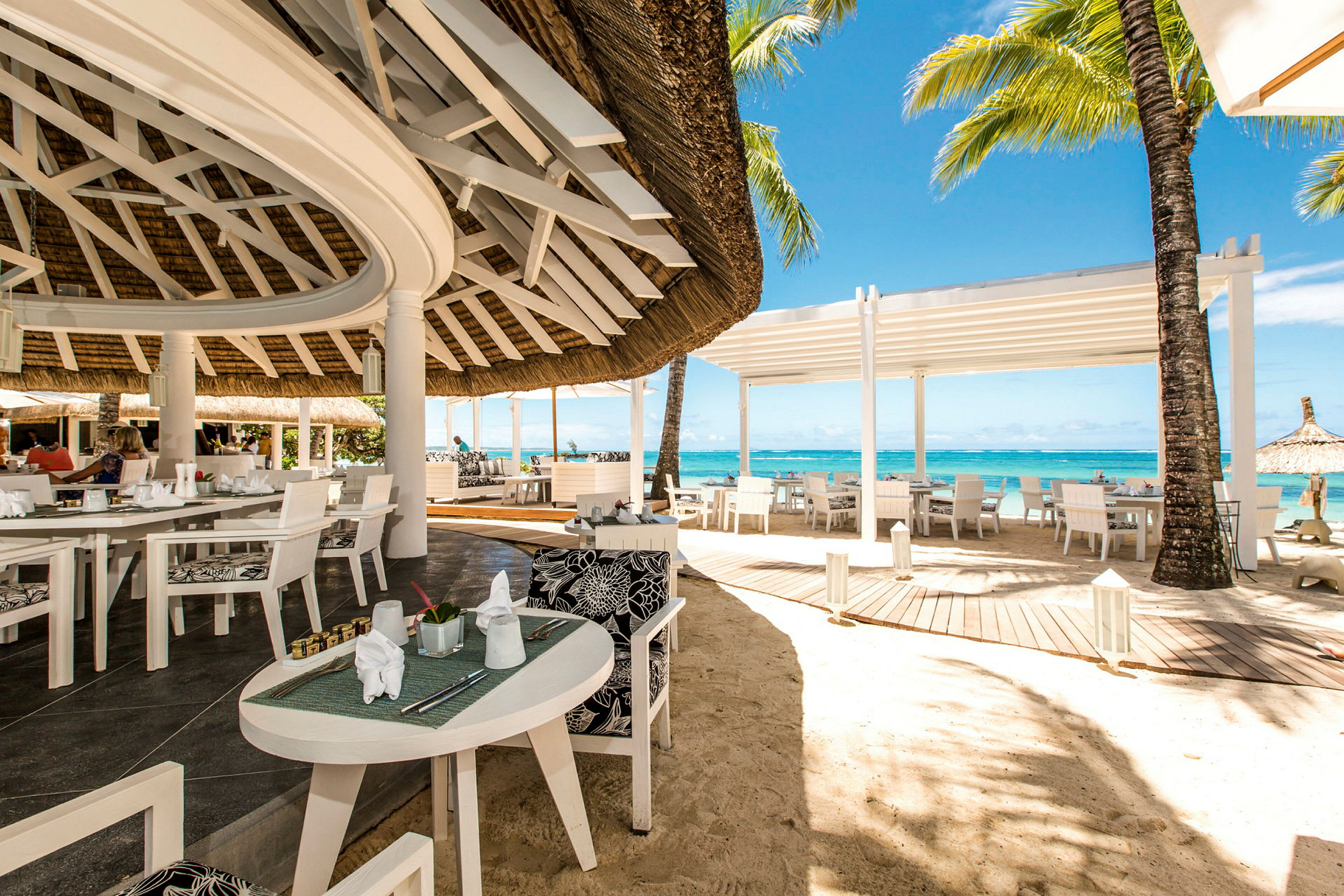 En åben restaurant ved stranden med hvide møbler og udsigt over havet. (AI-genereret tekst)