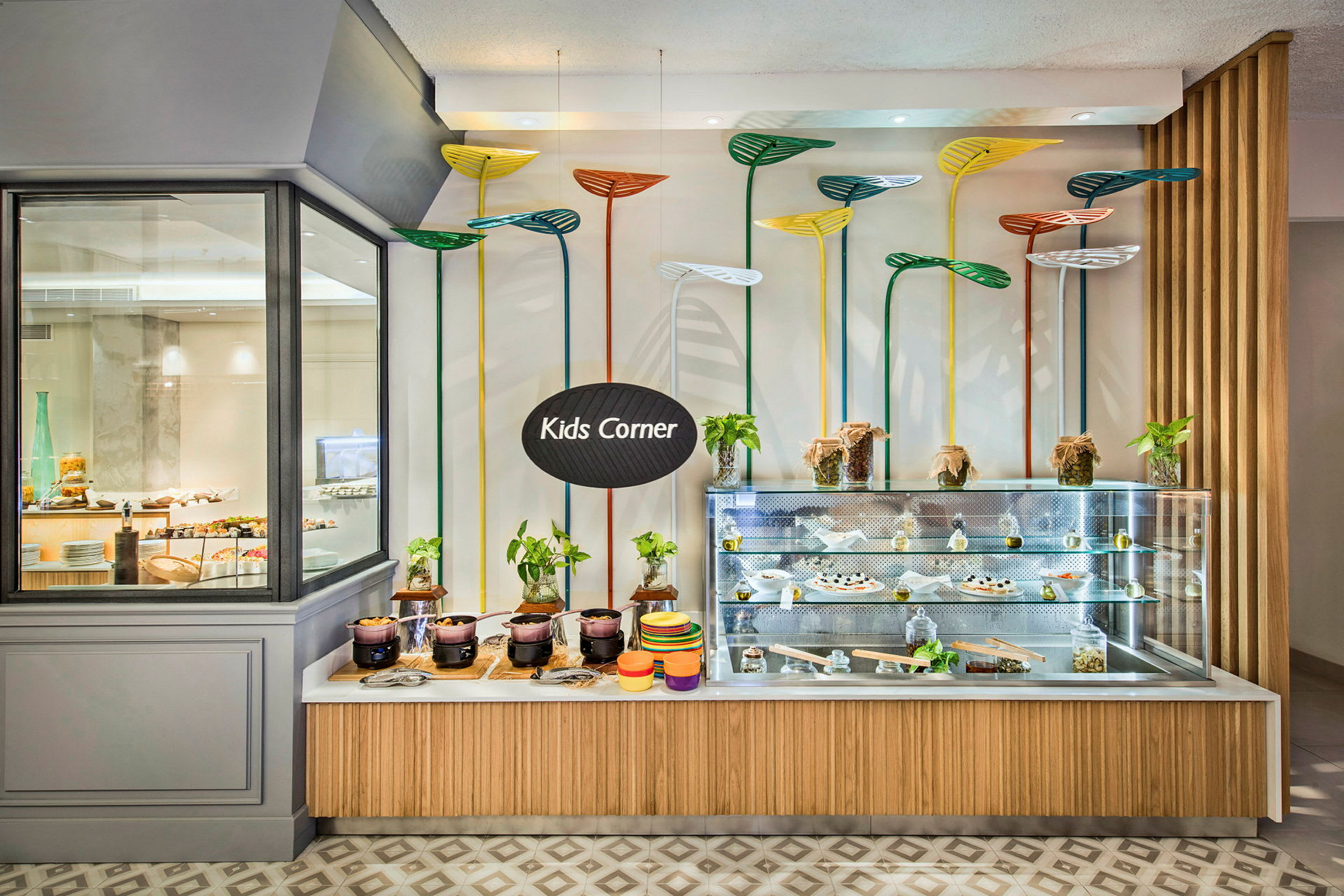 Et madområde for børn mærket med skiltet "Kids Corner" med en udstillingsdisk fyldt med måltider og dekoreret med farverige planteagtige designelementer. (AI-genereret tekst)