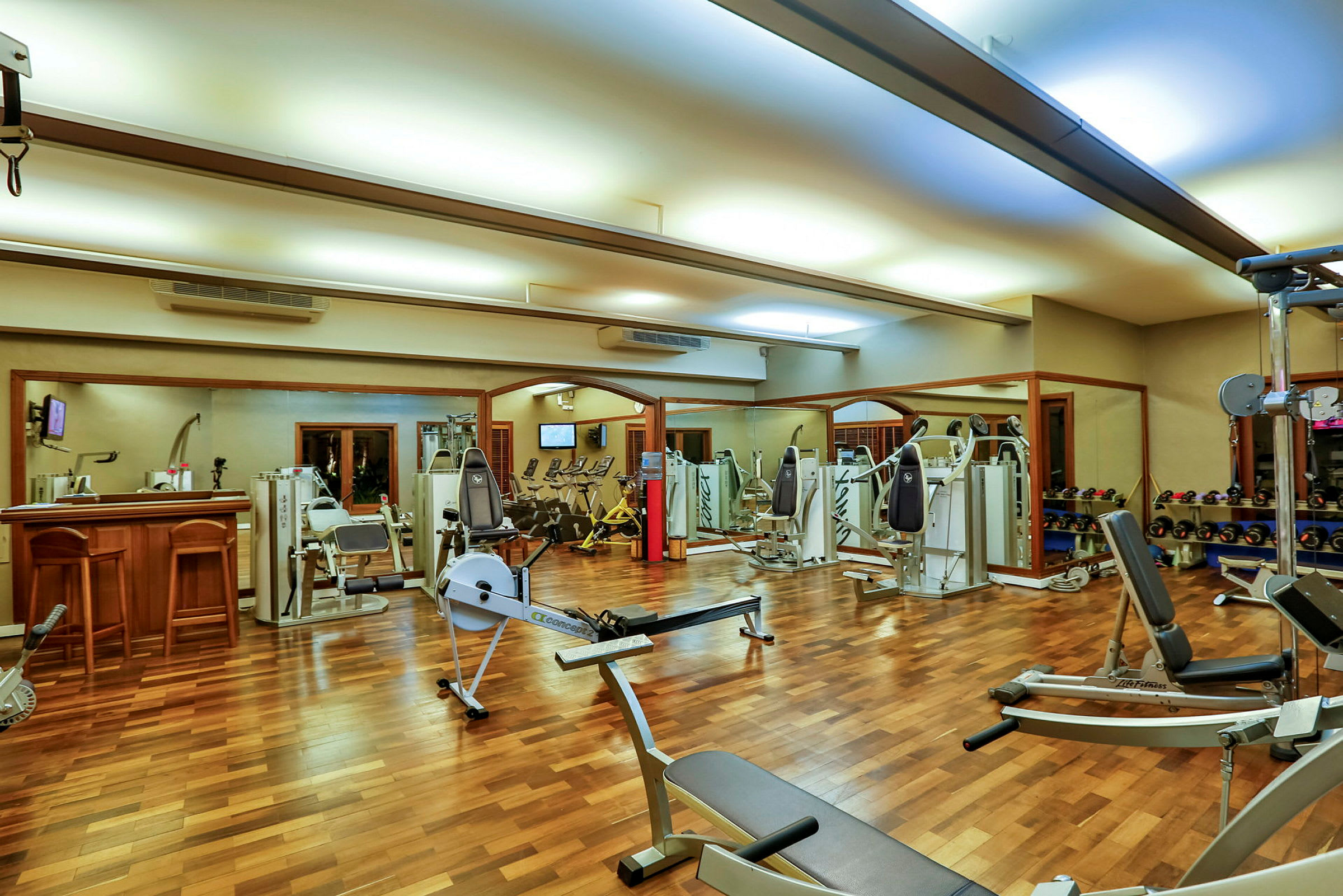 Et fitnesscenter med træningsmaskiner og frie vægte på et trægulv. (AI-genereret tekst)