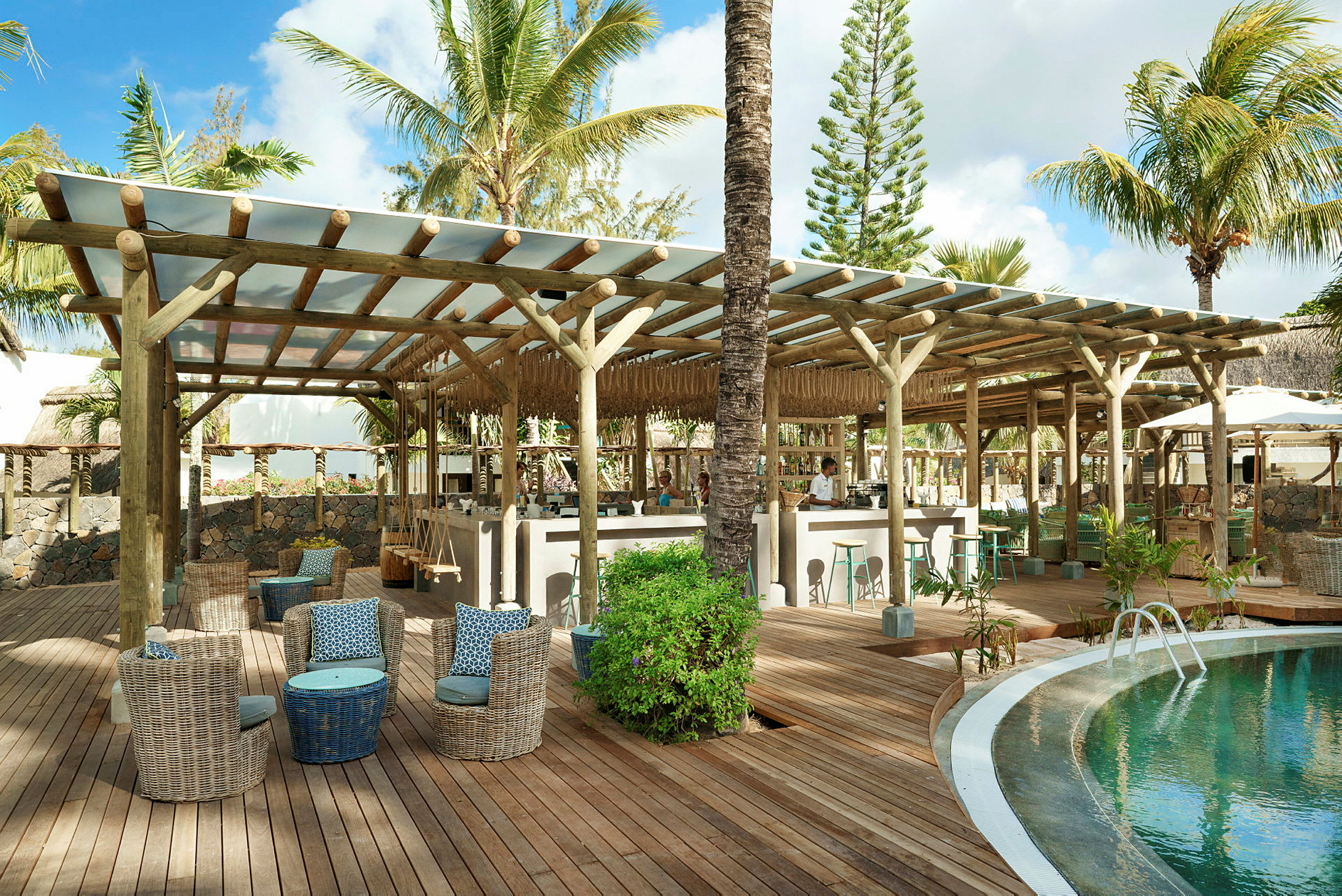 En lounge ved en pool på en tropisk resort med siddepladser og en bar under træbjælker. (AI-genereret tekst)