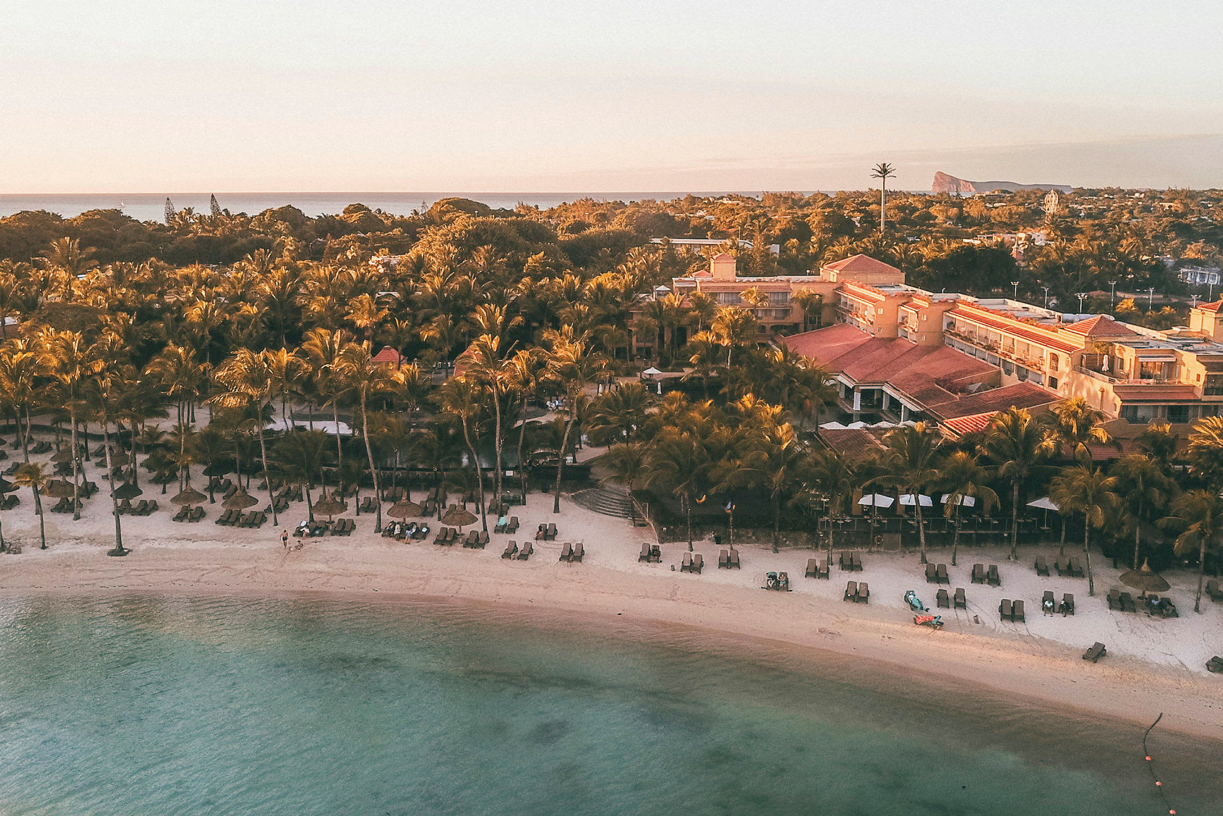 Strand med liggestole og parasoller foran en resort og palmer ved havet. (AI-genereret tekst)