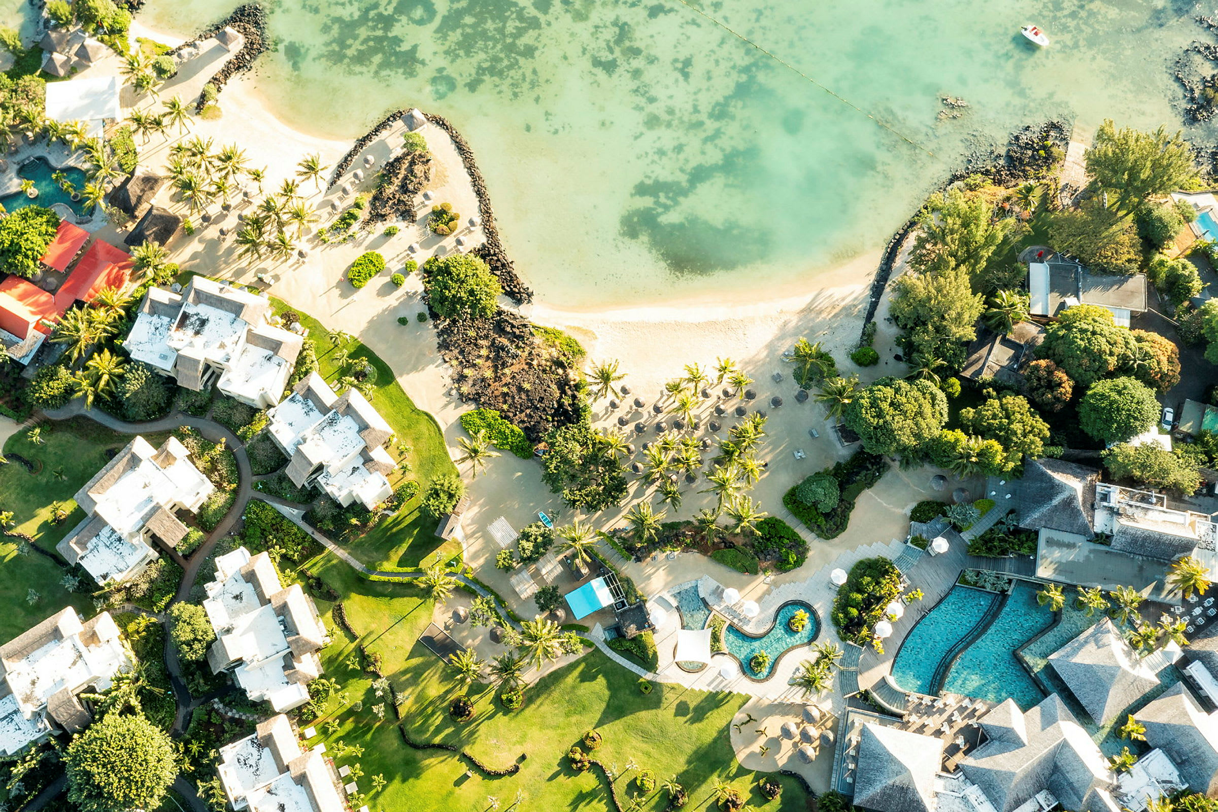 Luftfoto af hotelbygninger og poolområder langs en sandstrand med palmer. (AI-genereret tekst)
