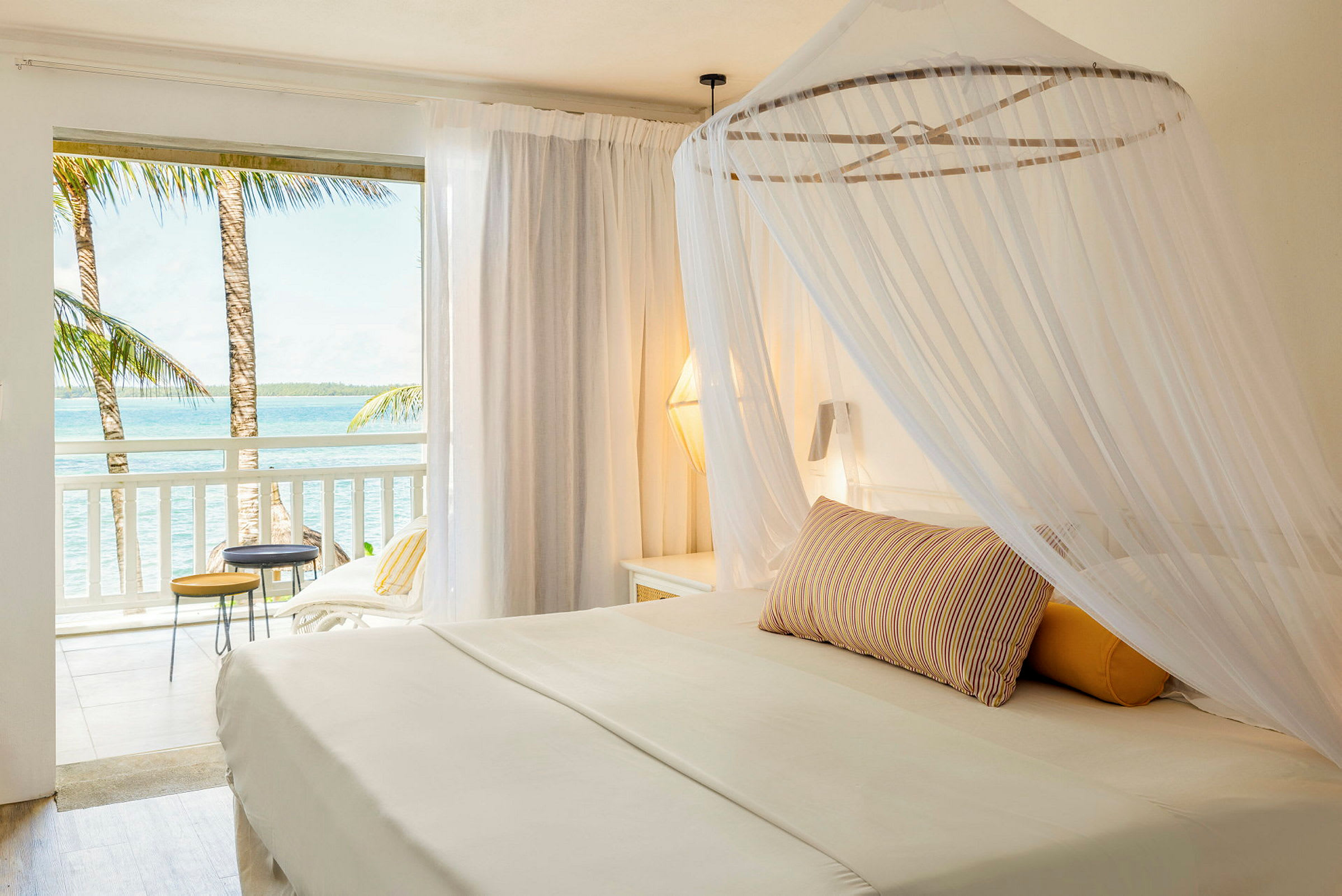 En lys hotelsuite med en himmelseng og udsigt over havet fra altanen. (AI-genereret tekst)