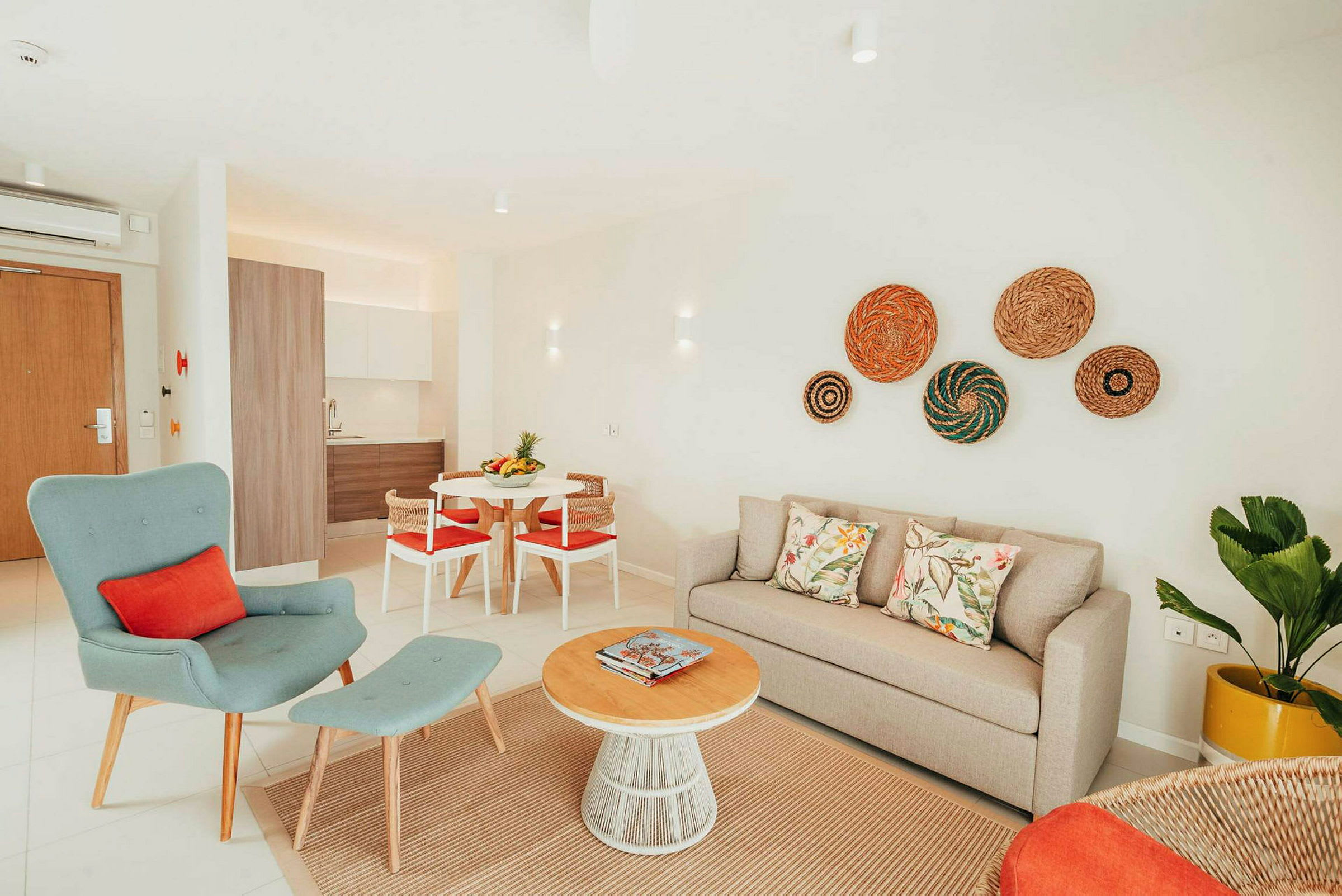 En lys og moderne indrettet stue med beige sofa, grøn lænestol og et rundt sofabord af træ. Køkkenet er synligt i baggrunden. (AI-genereret tekst)