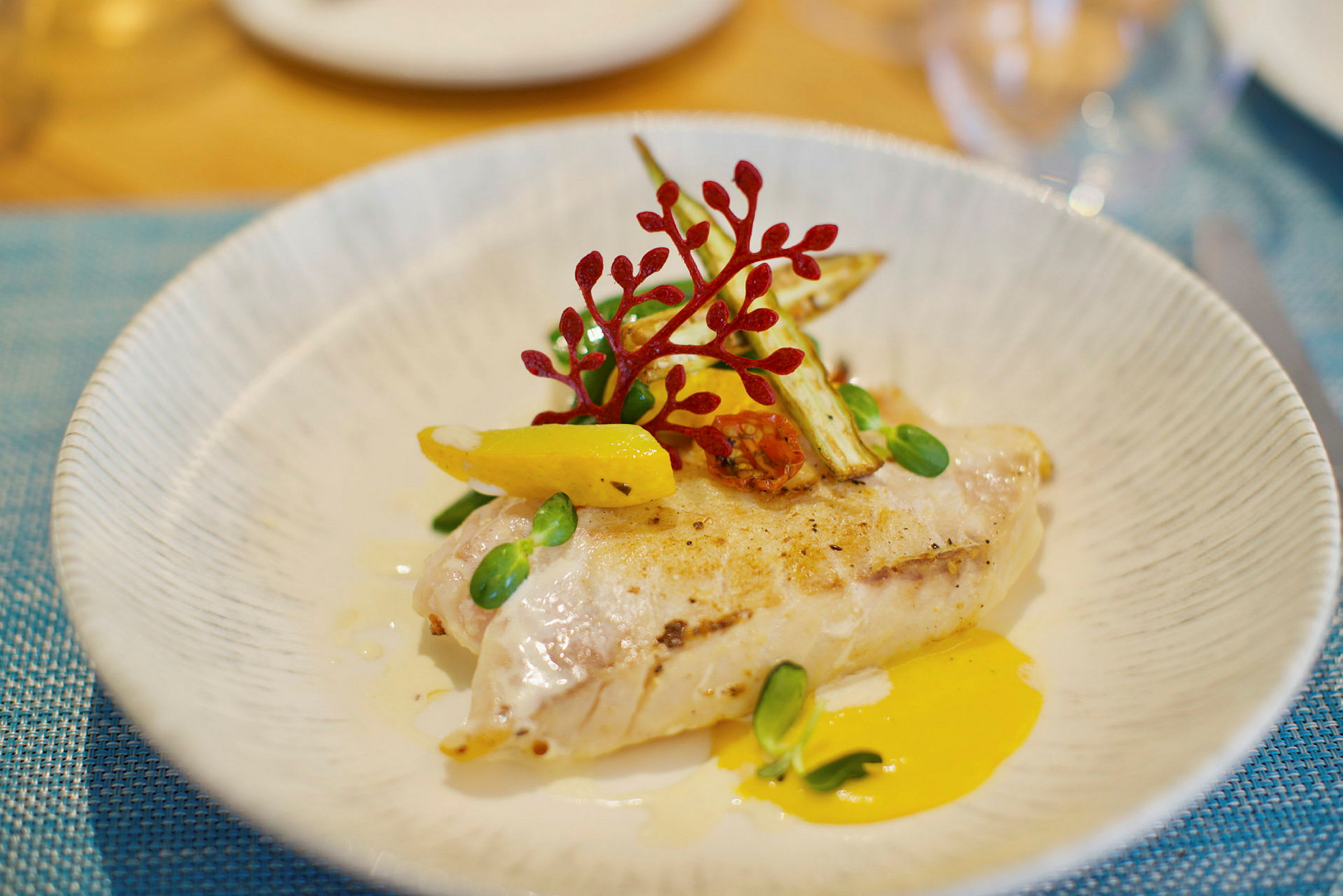 En tallerken med en elegant anrettet ret bestående af grillet fiskefilet med grøntsager og sauce. (AI-genereret tekst)