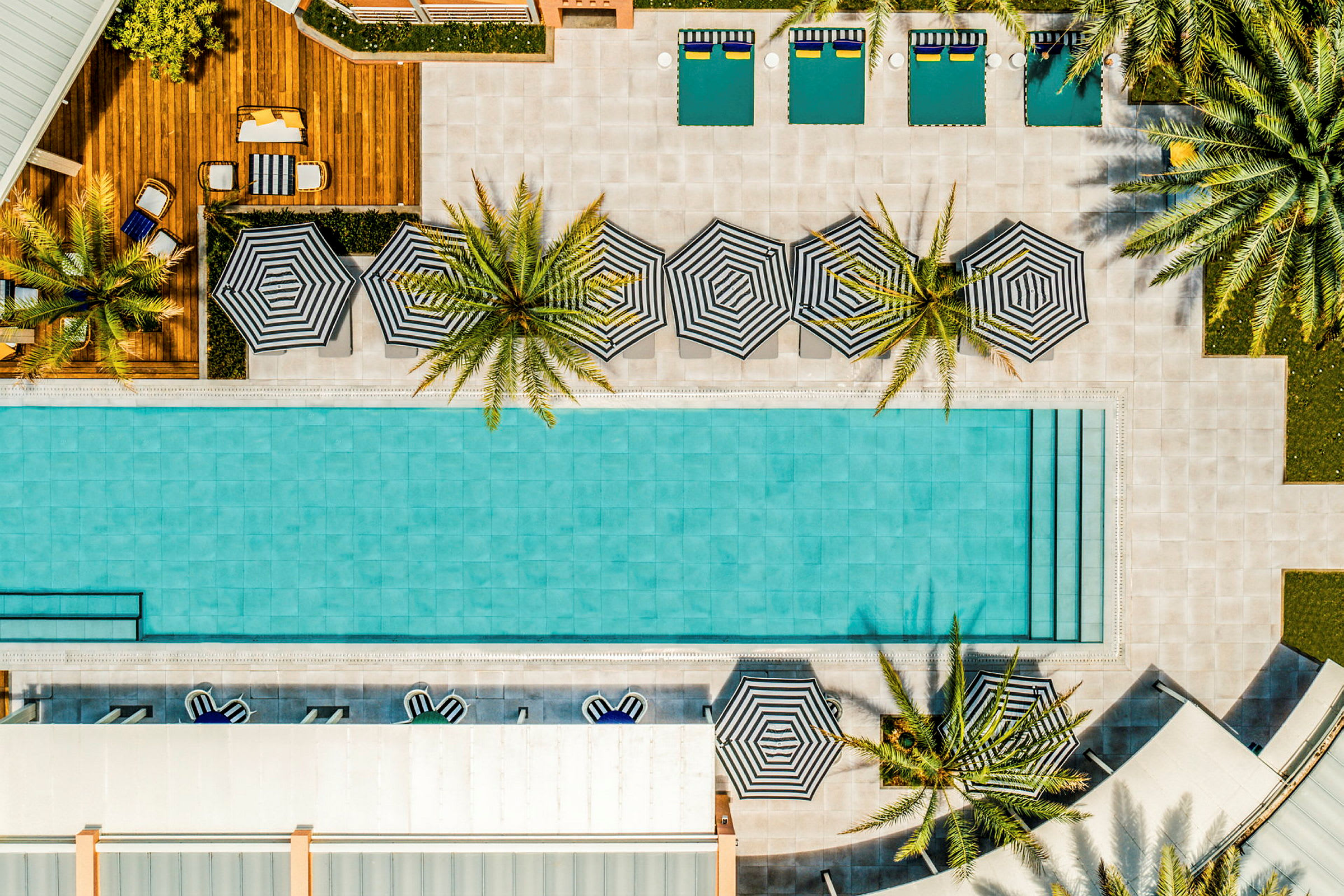 Luftfoto af en pool med liggestole og parasoller omgivet af palmer. (AI-genereret tekst)