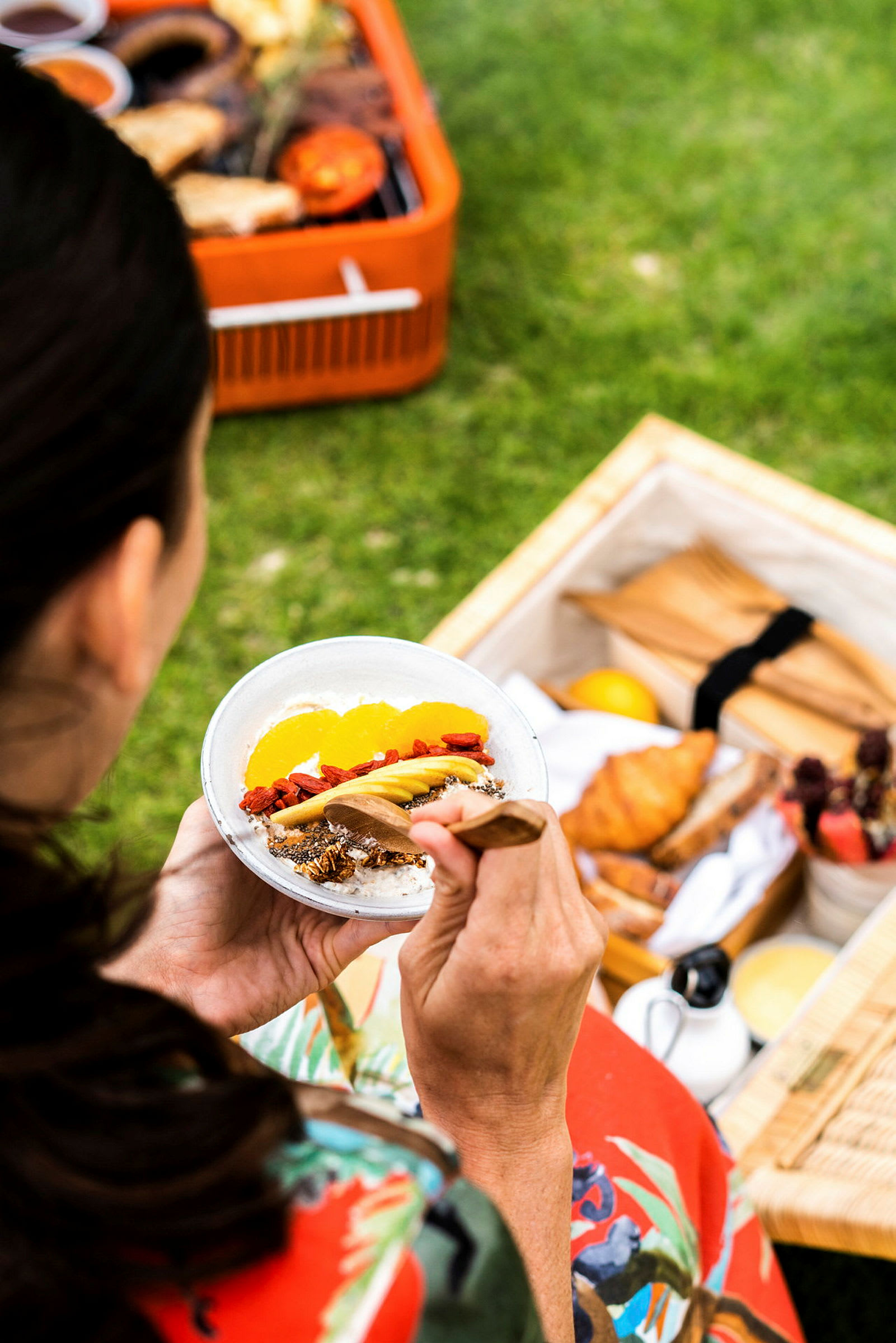 En person holder en tallerken med yoghurt og frugt, omgivet af en picnicopstilling udendørs. (AI-genereret tekst)