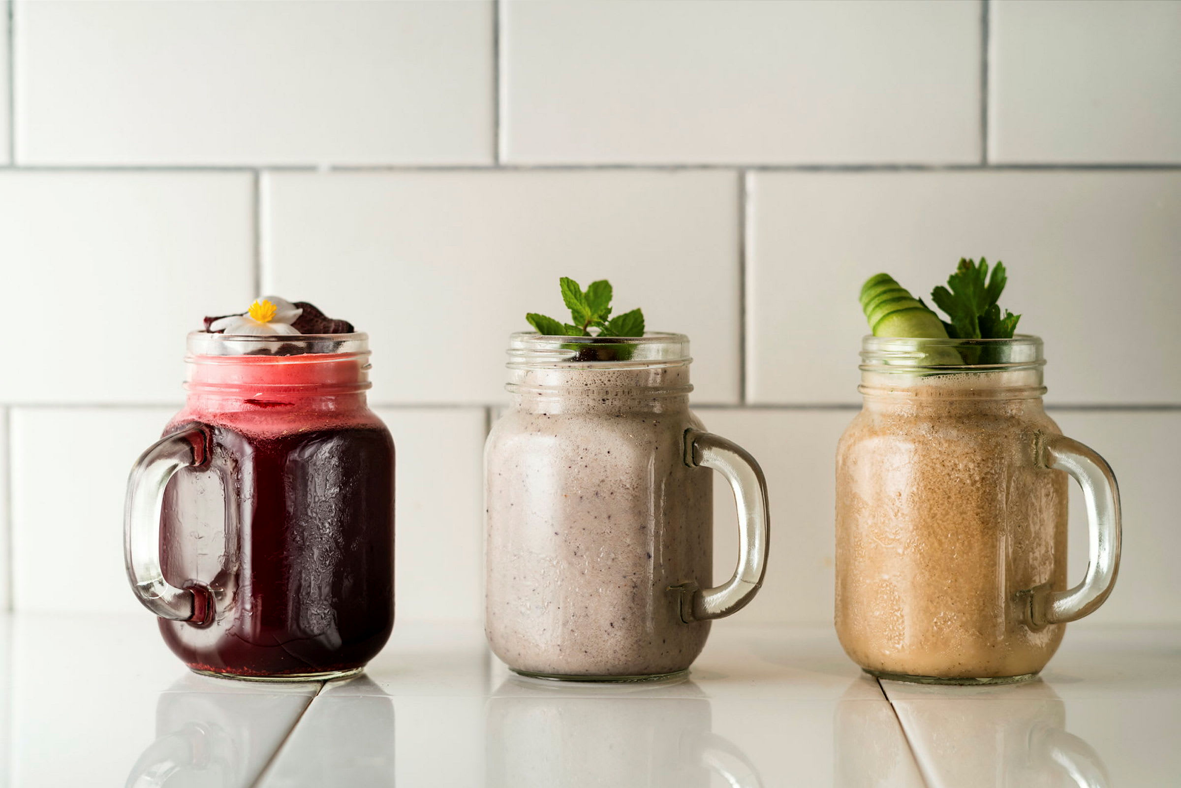 Tre forskellige smoothies i glasbeholdere på en hvid overflade. (AI-genereret tekst)