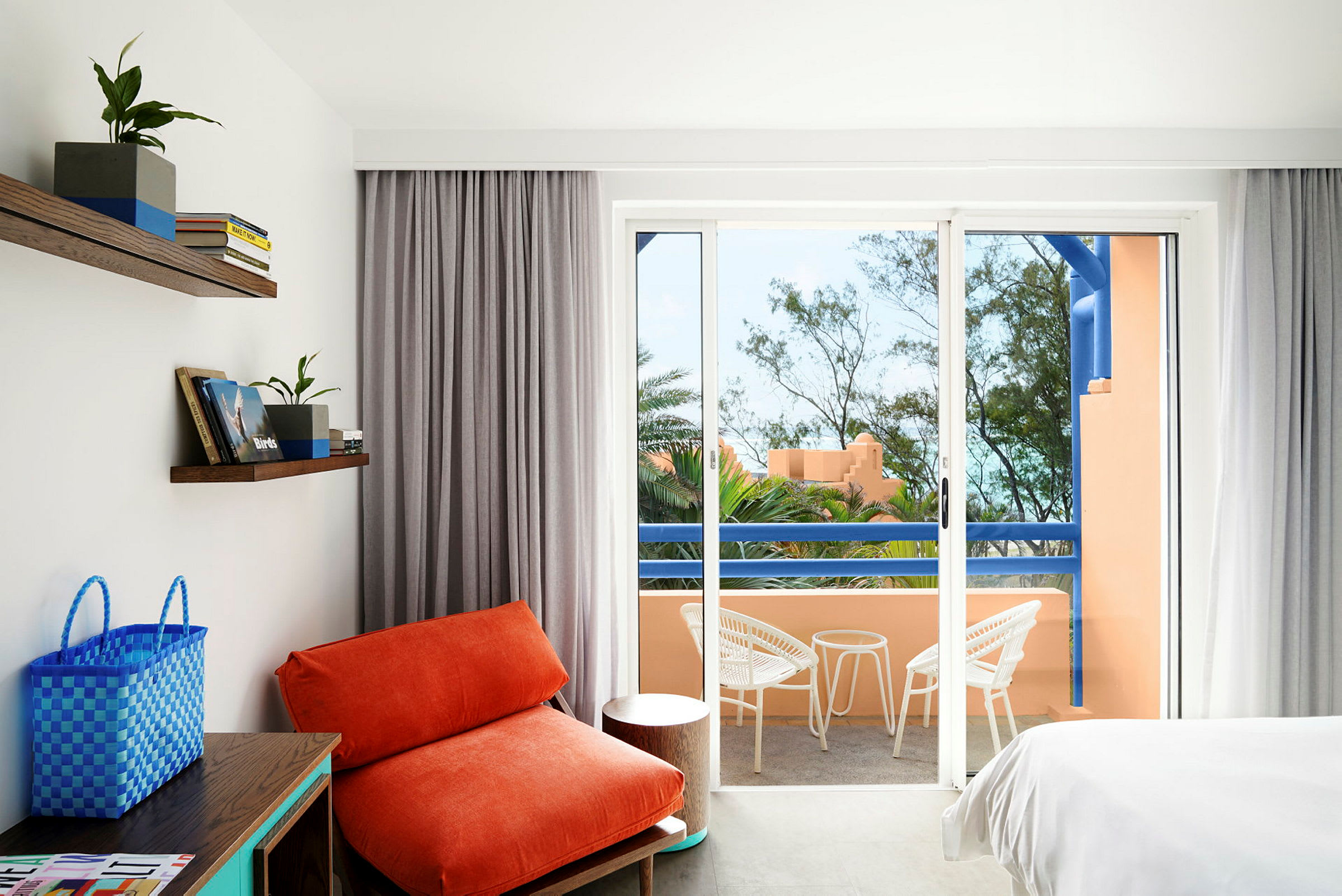 Et hotelværelse med en orange lænestol, hvide møbler på en balkon og udsigt over grønne områder. (AI-genereret tekst)