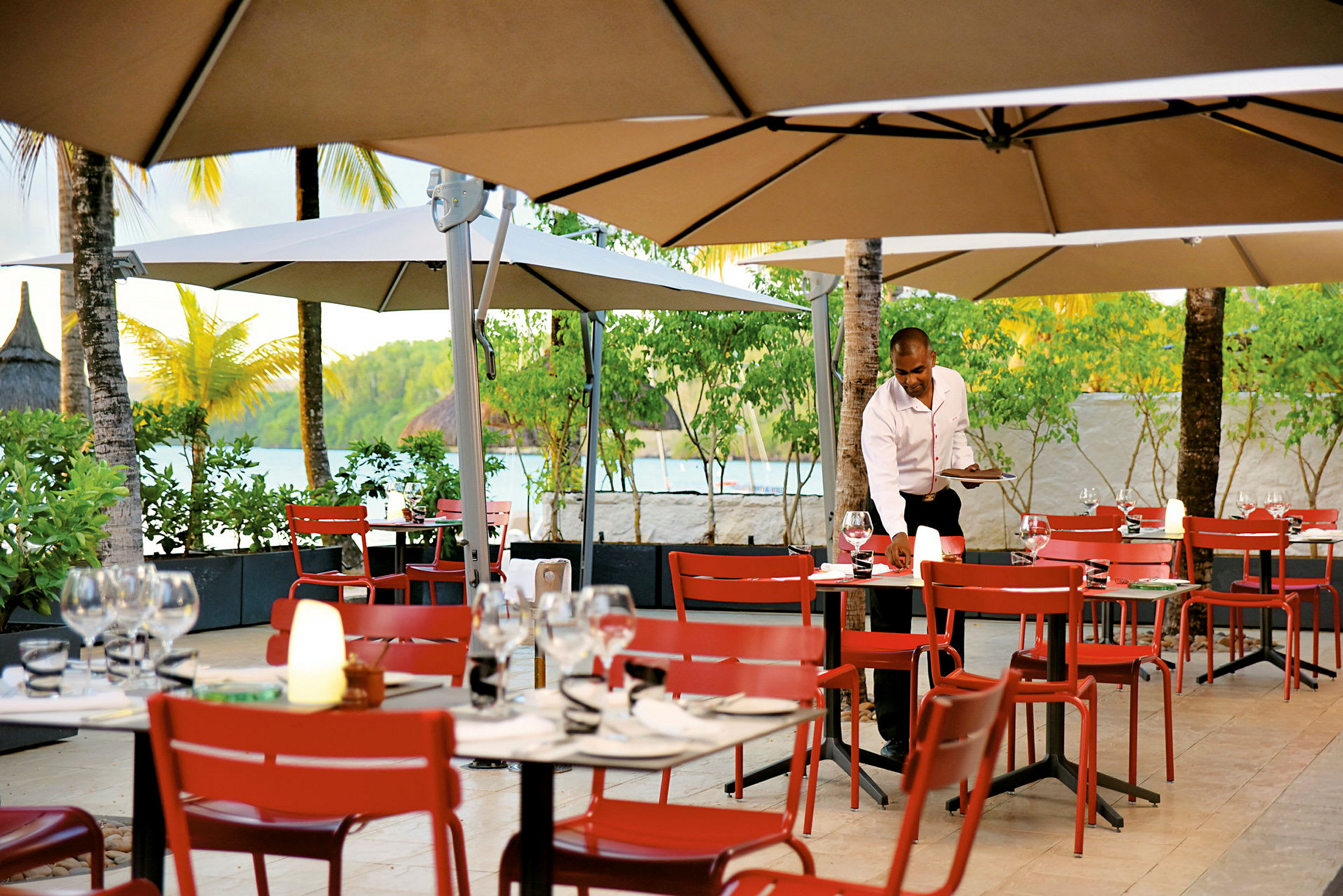 Restaurant med udendørs servering, røde stole og borde under parasoller. (AI-genereret tekst)