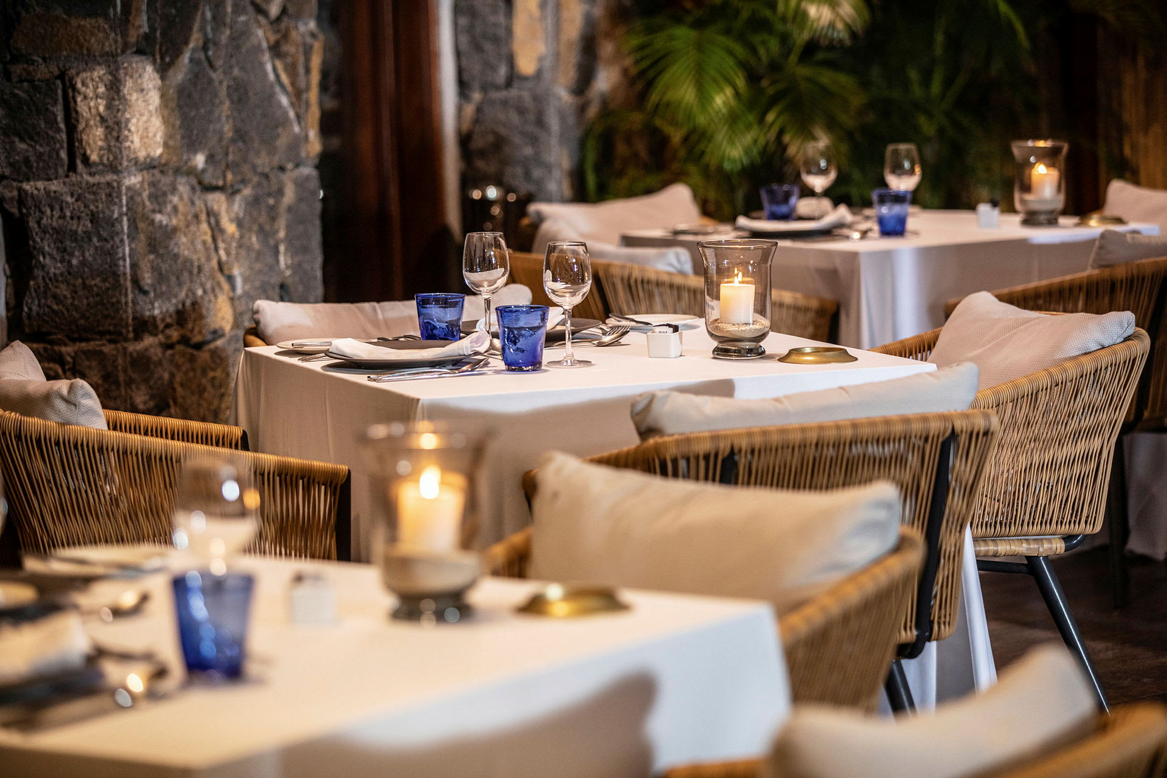 Et elegant opdækket bord i en restaurant med rottingstole og hvide linnedug. (AI-genereret tekst)