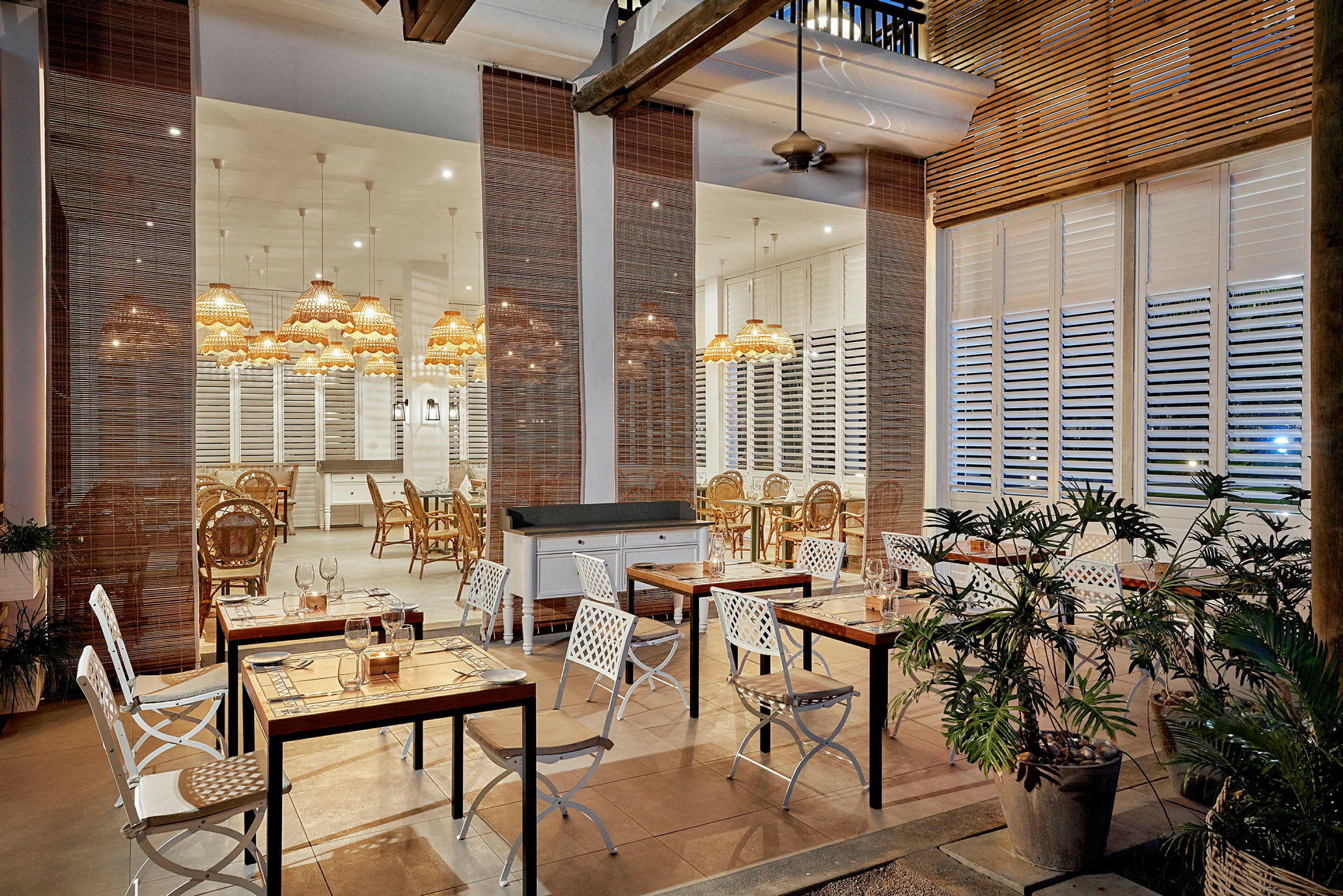 Indretning af en restaurant med borde og stole i forskellige sektioner, omgivet af planter og med belysning fra designlamper. (AI-genereret tekst)