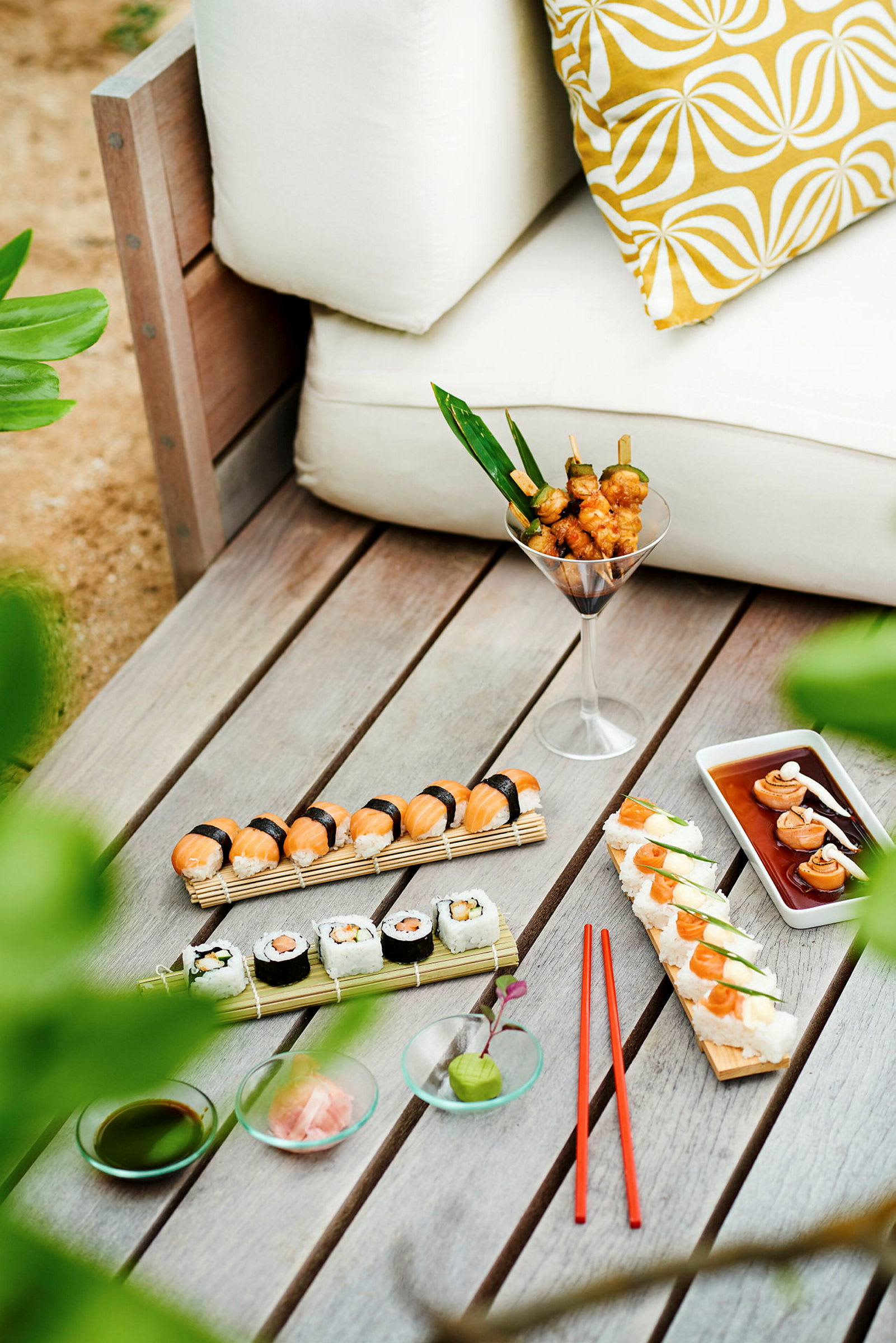 Et bord med sushi, grillspyd og tilbehør ved siden af en hvid sofa. (AI-genereret tekst)