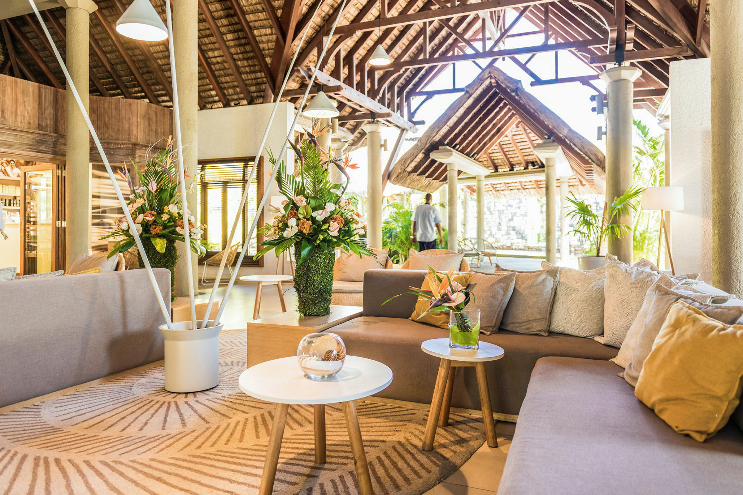 Interiøret i en rummelig og lys lounge med sofaer, blomster og tagbjælker. (AI-genereret tekst)