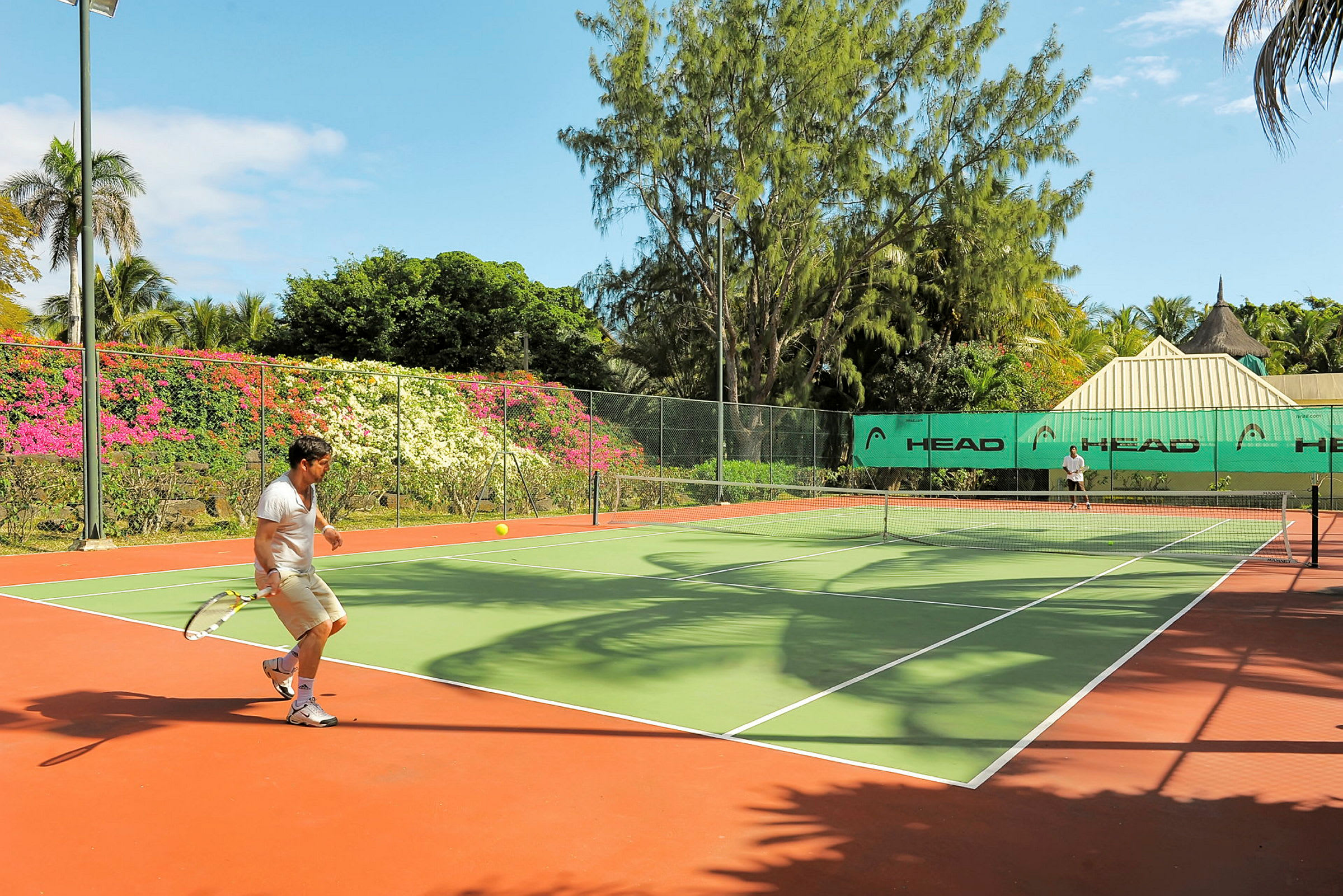 En tennisbane omgivet af grønne områder og farverige blomster. (AI-genereret tekst)