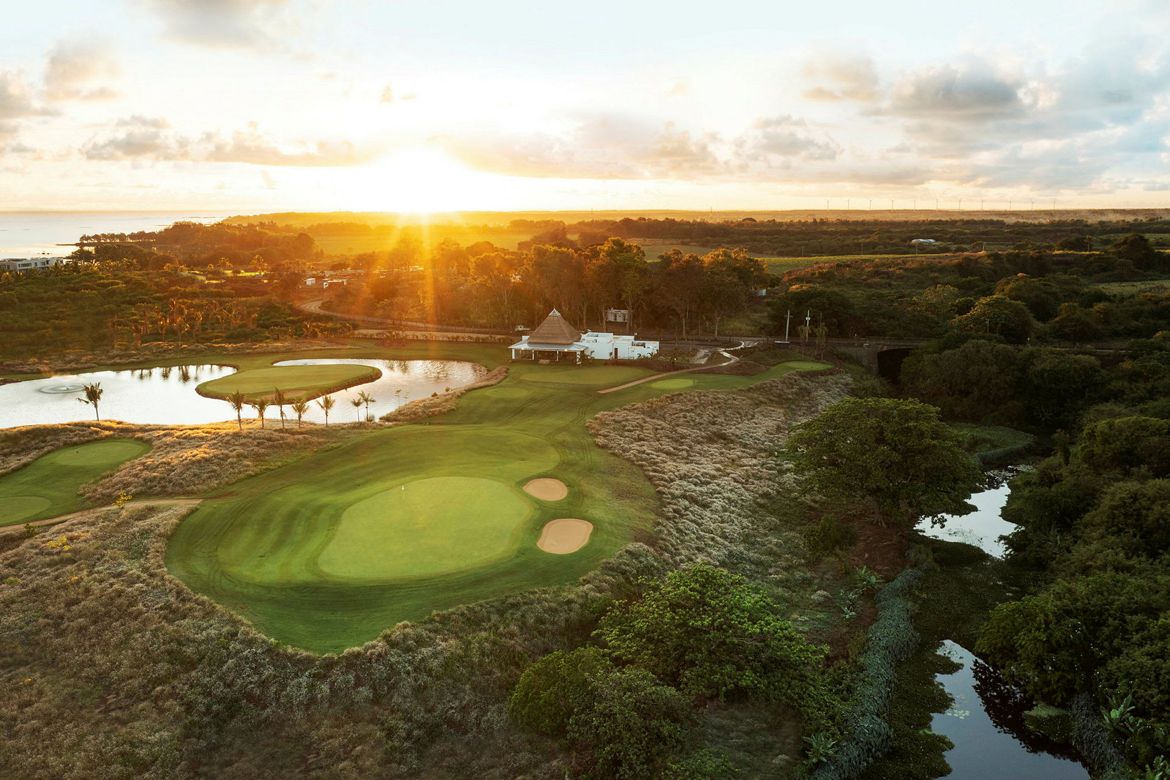 En golfbane med grønne fairways, bunkers og en dam, omgivet af vegetation under solnedgang. (AI-genereret tekst)