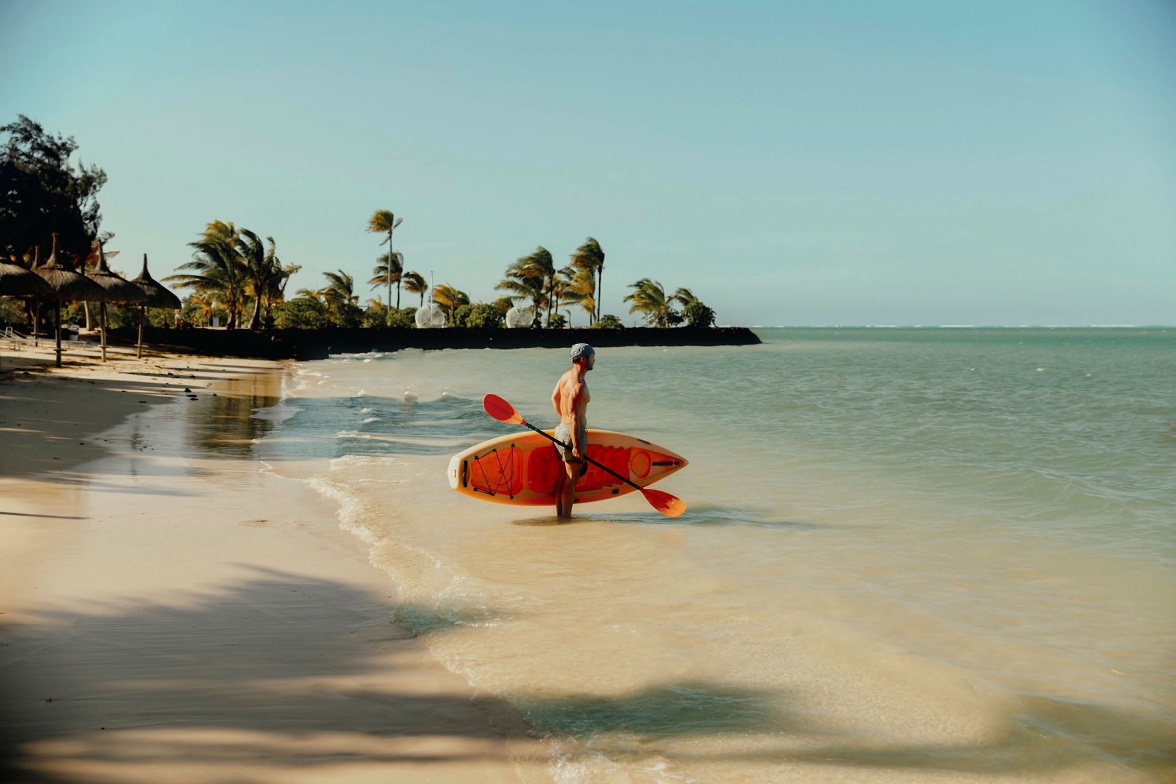En person står på en sandstrand med et paddleboard og en paddel ved vandet. (AI-genereret tekst)