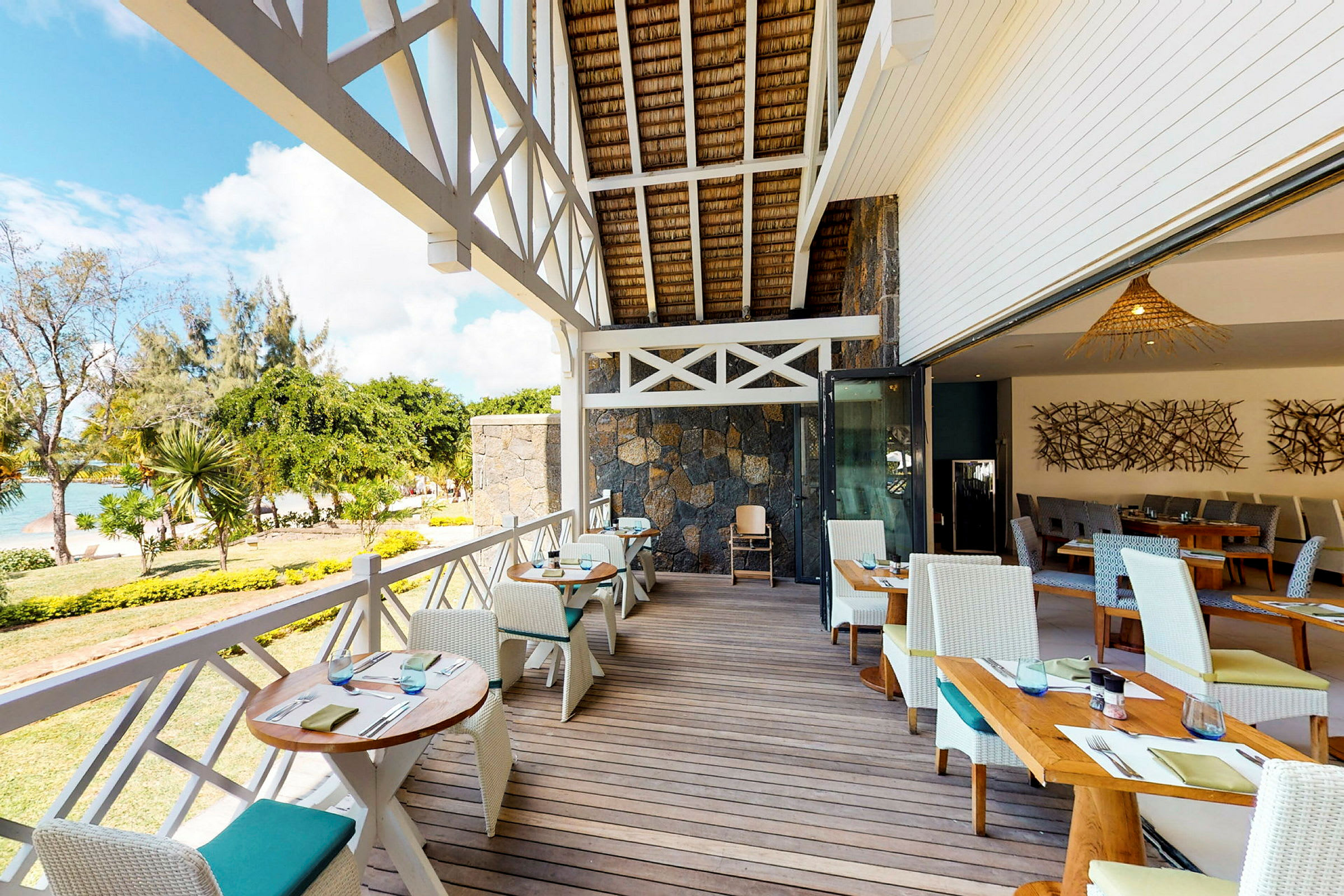 Udendørs servering med borde og stole på en terrasse med udsigt over strand og hav. (AI-genereret tekst)