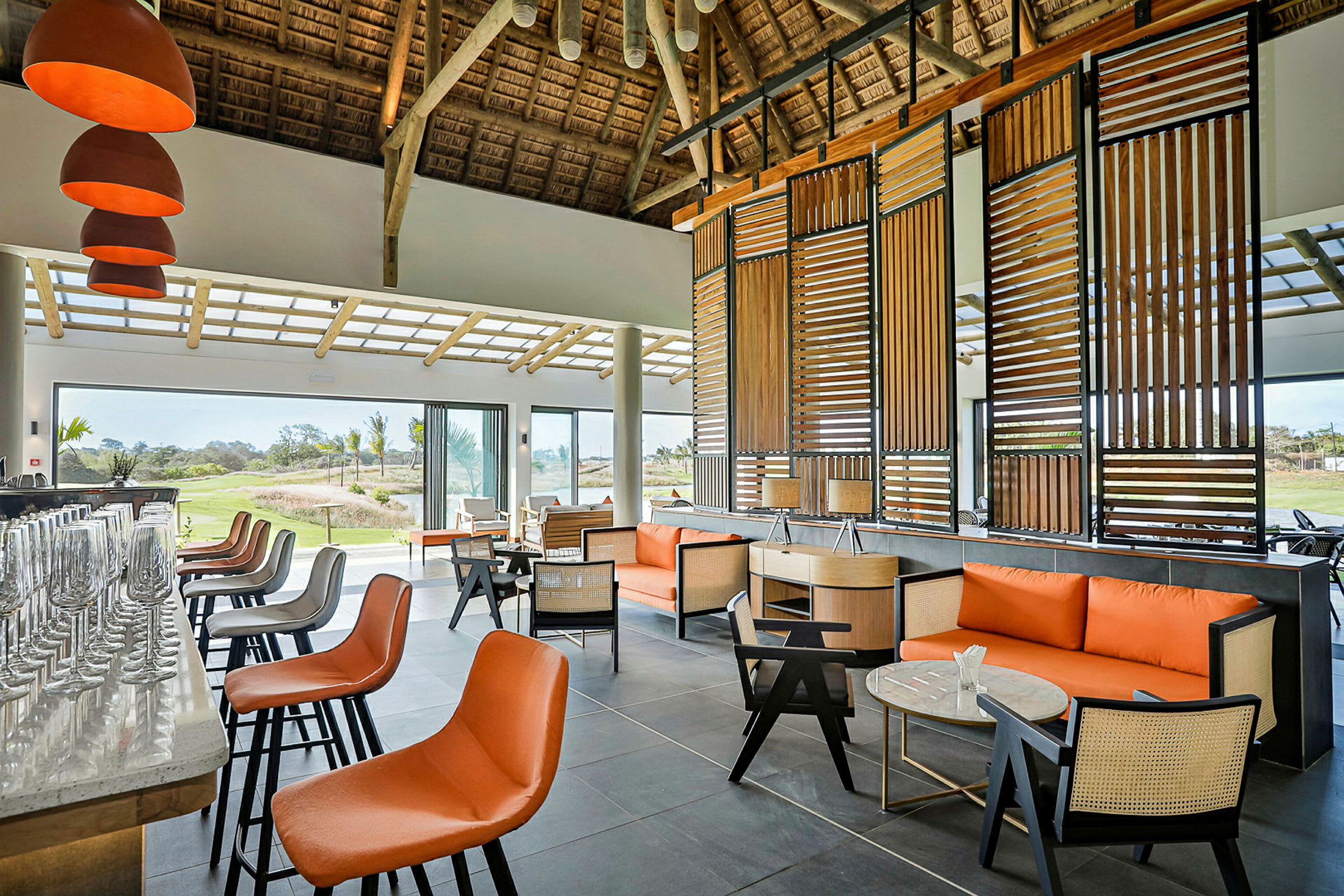 Interiør af en moderne lounge med store vinduer, orange og sorte møbler samt en bardisk. (AI-genereret tekst)