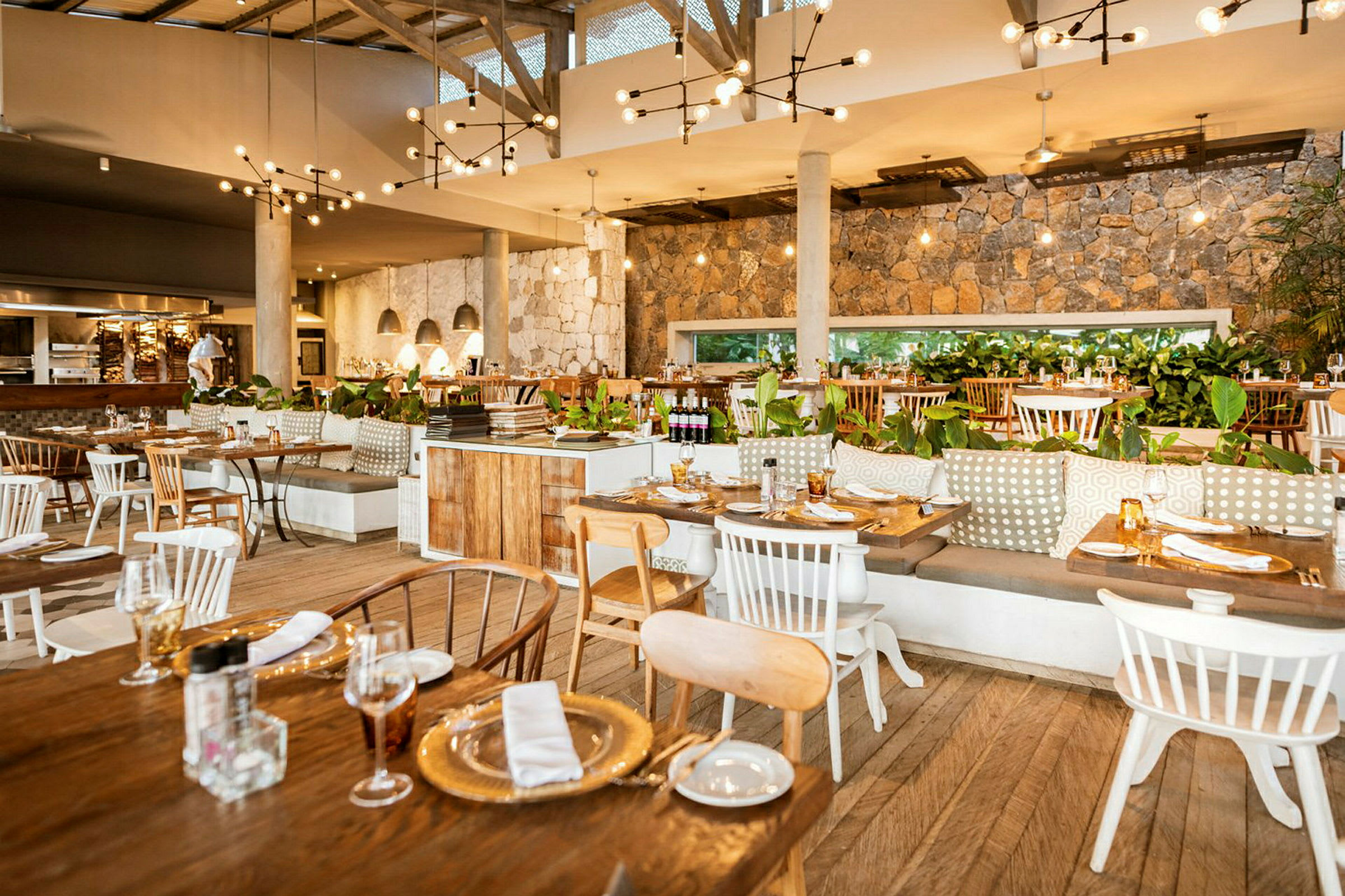 Indendørs interiør af en restaurant med træborde og stole, stenvægge, hængende lamper og grønne planter som dekoration. (AI-genereret tekst)