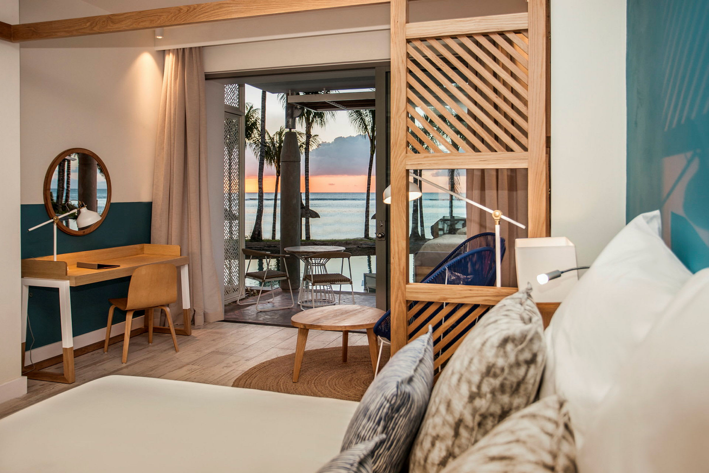Interiøret i et hotelværelse med en seng, skrivebord og udsigt over havet og solnedgangen. (AI-genereret tekst)