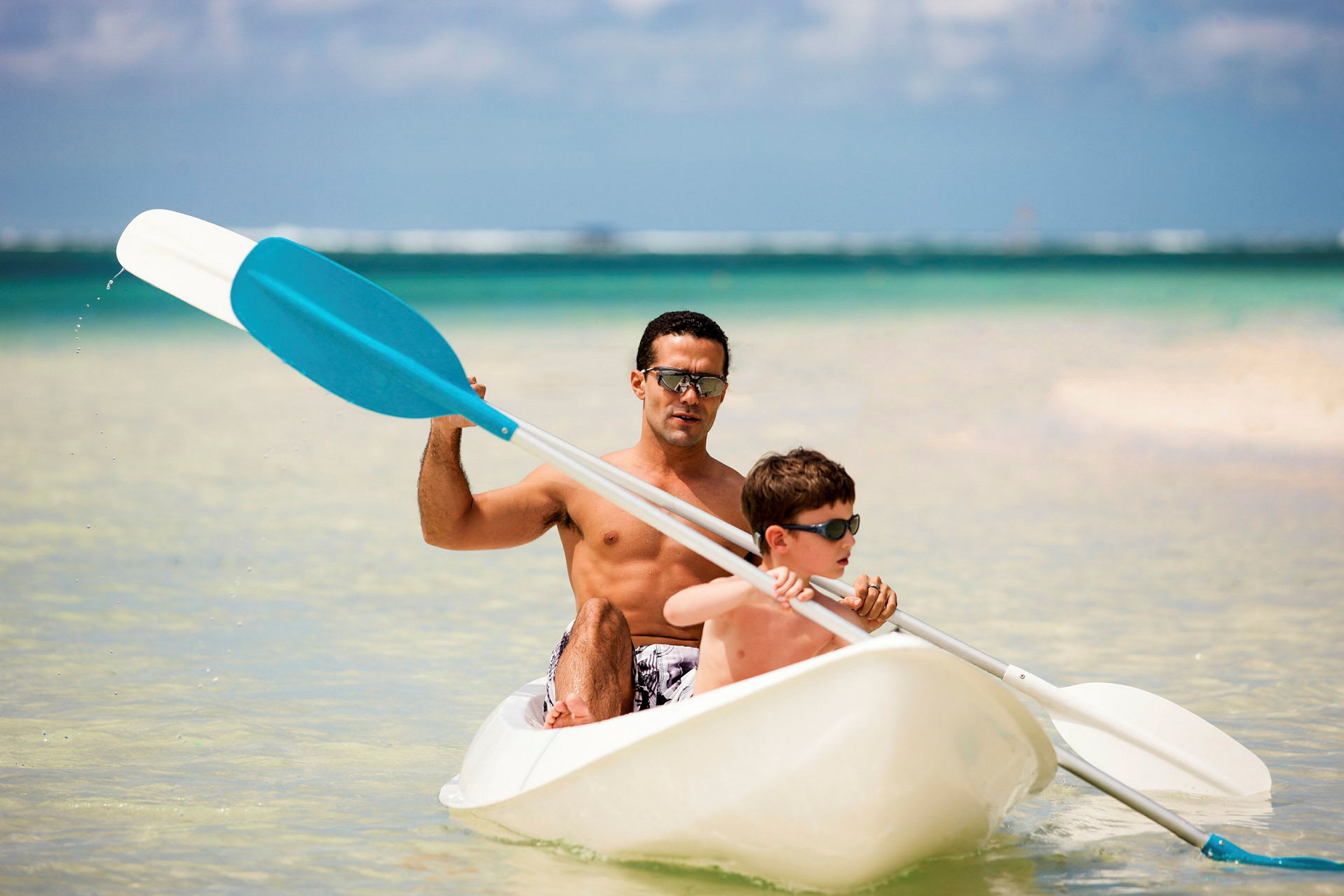 To personer padler en kajak i klart vand ved en strand. (AI-genereret tekst)