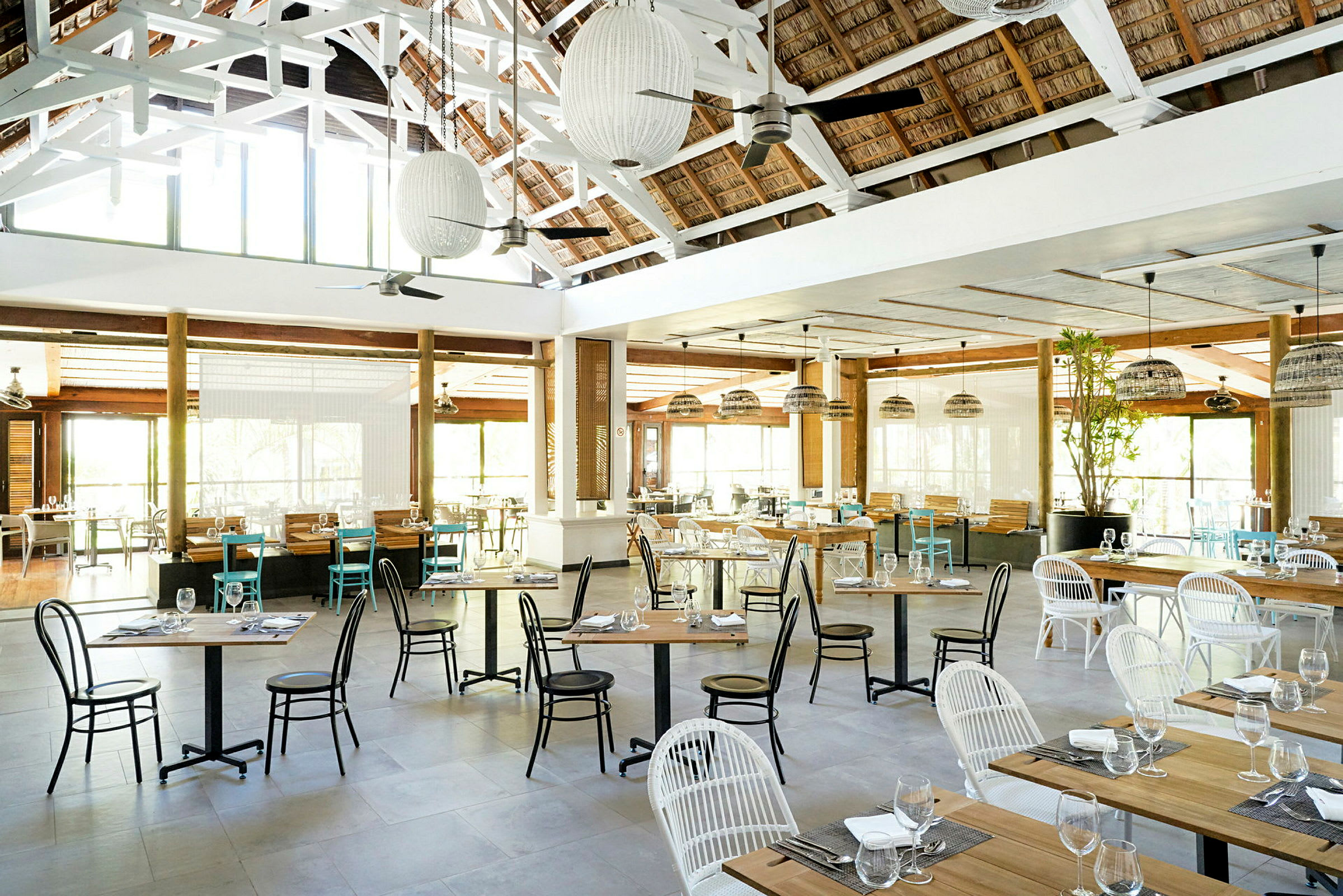 En rummelig restaurant med borde og stole, dekoreret med lamper og store vinduer, der lukker lys ind. (AI-genereret tekst)