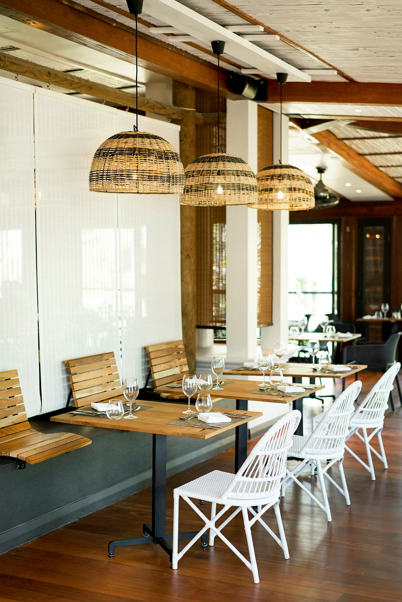 En restaurant med træborde, hvide stole og hængende lamper af rattan. (AI-genereret tekst)