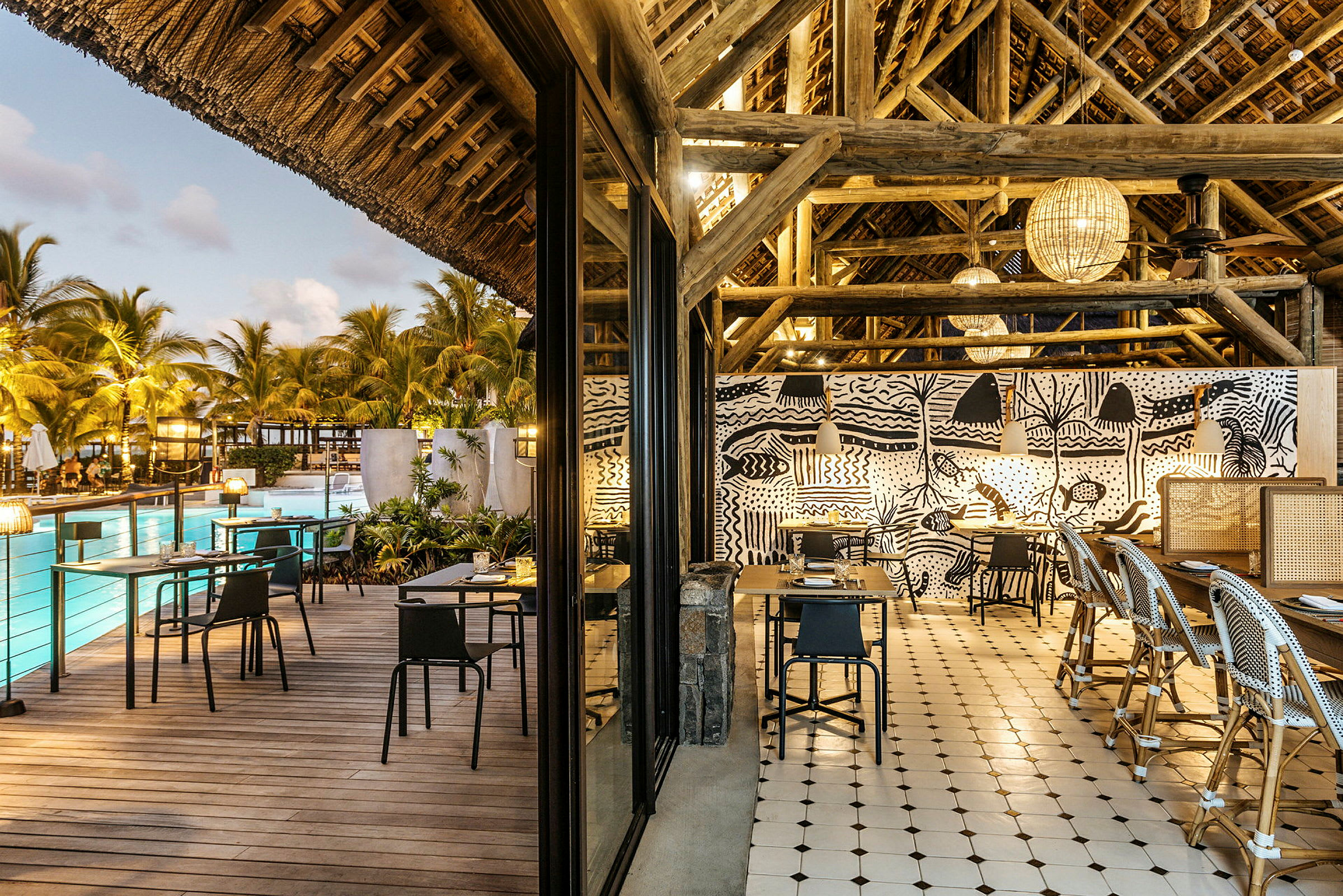 En restaurant med åben siddeplads, med moderne design og pool og palmer synlige i baggrunden. (AI-genereret tekst)