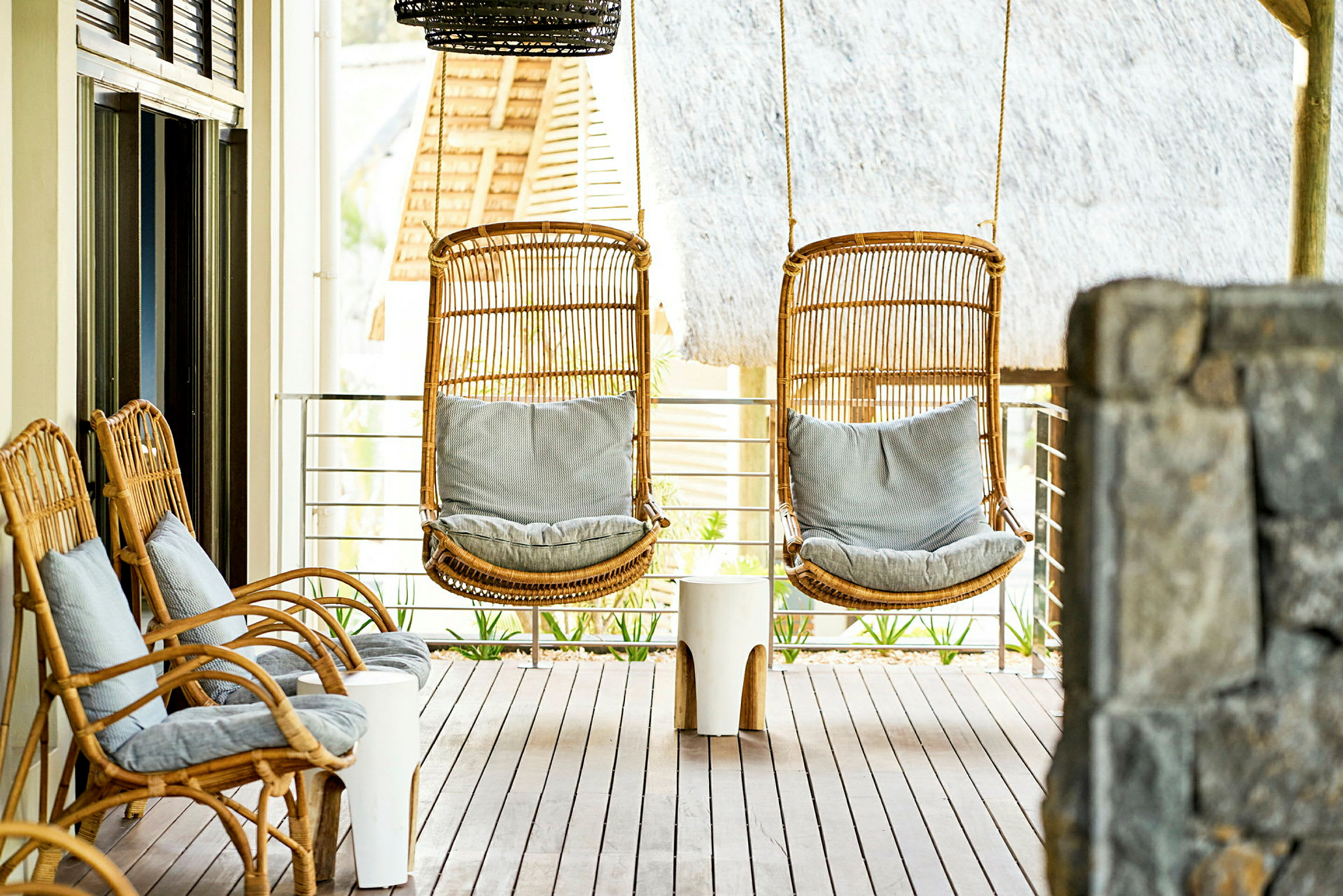 To hængestole og tre sidestole i rattan med puder på en terrasse. (AI-genereret tekst)