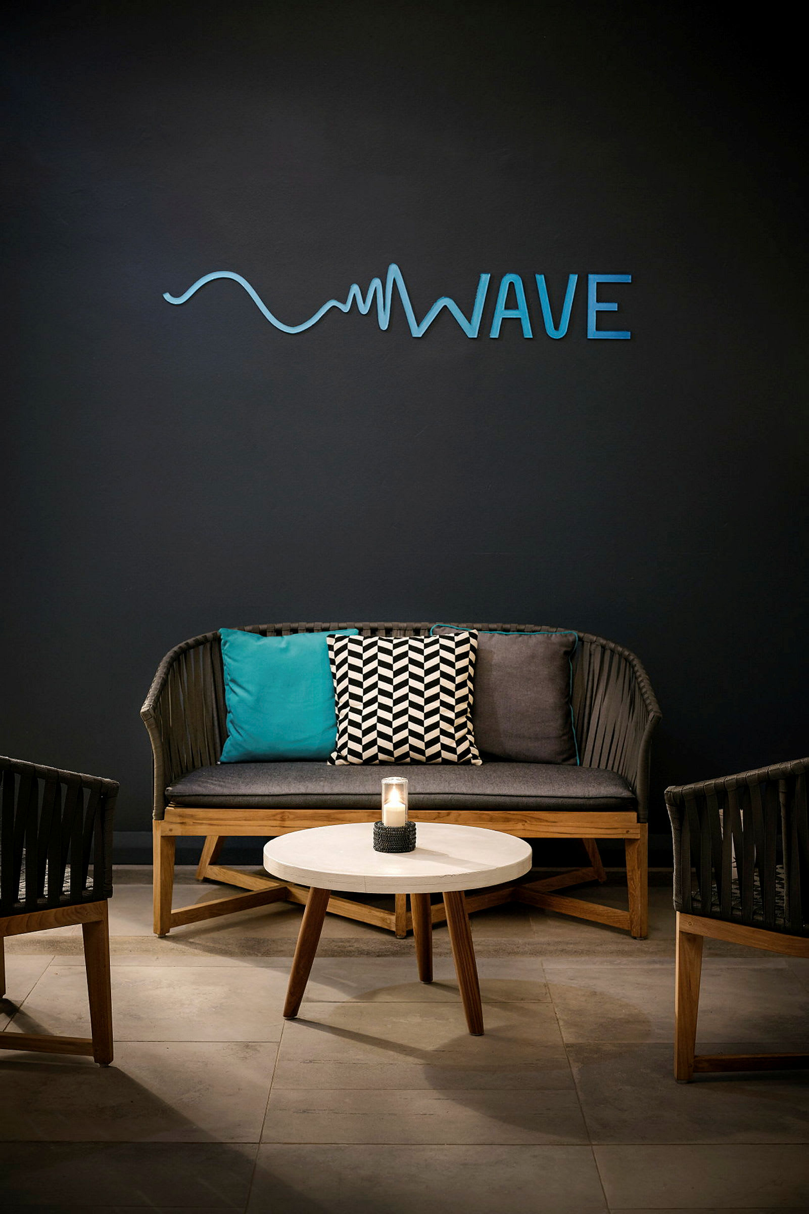 En siddegruppe med en sofa, to stole, et rundt bord og en væg med teksten 'Wave'. (AI-genereret tekst)