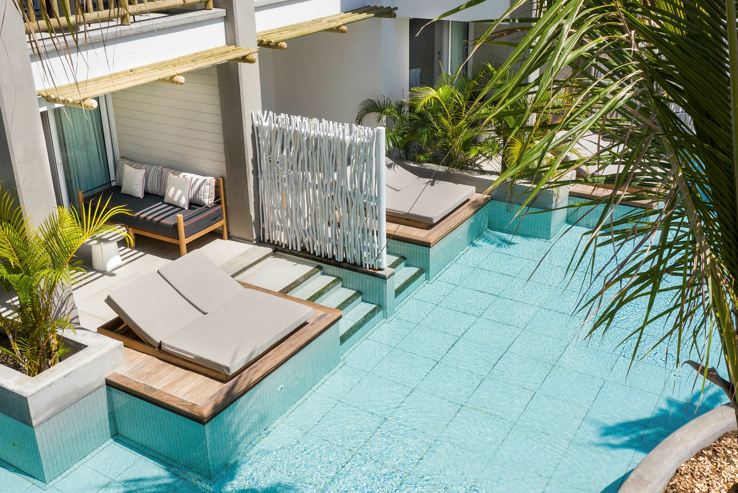 Hotelværelse med udsigt over en pool, liggestole og grøn bevoksning. (AI-genereret tekst)