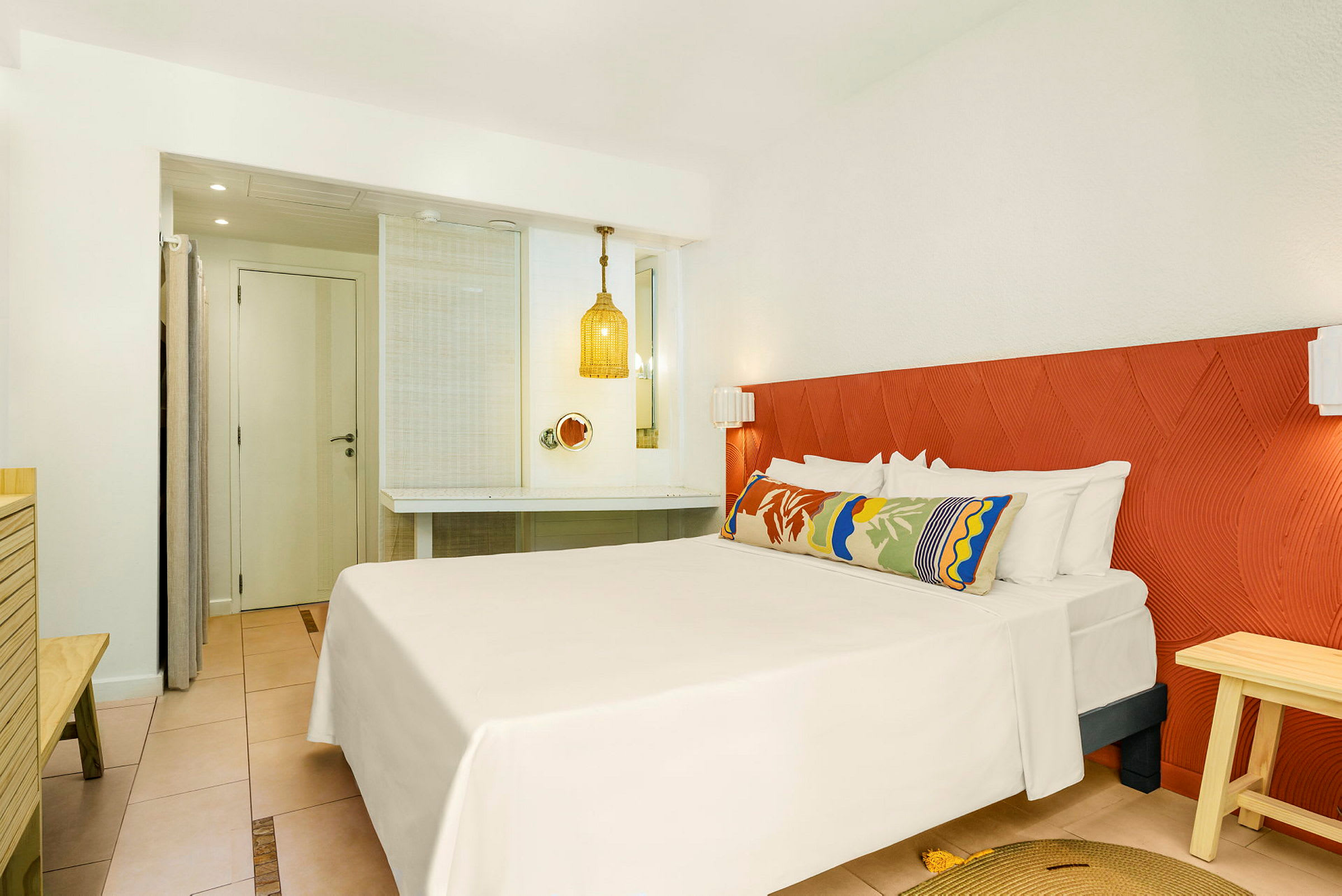 Hotelværelse med en dobbeltseng, farverig pude og en orange sengegavl. (AI-genereret tekst)