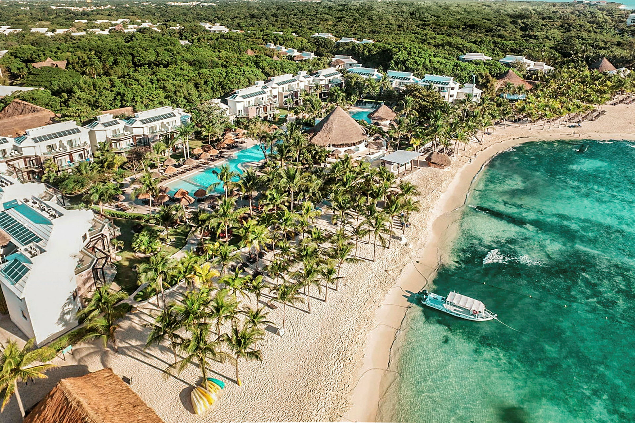 Hotelområde med pools og haver ved en sandstrand med turkis vand. (AI-genereret tekst)