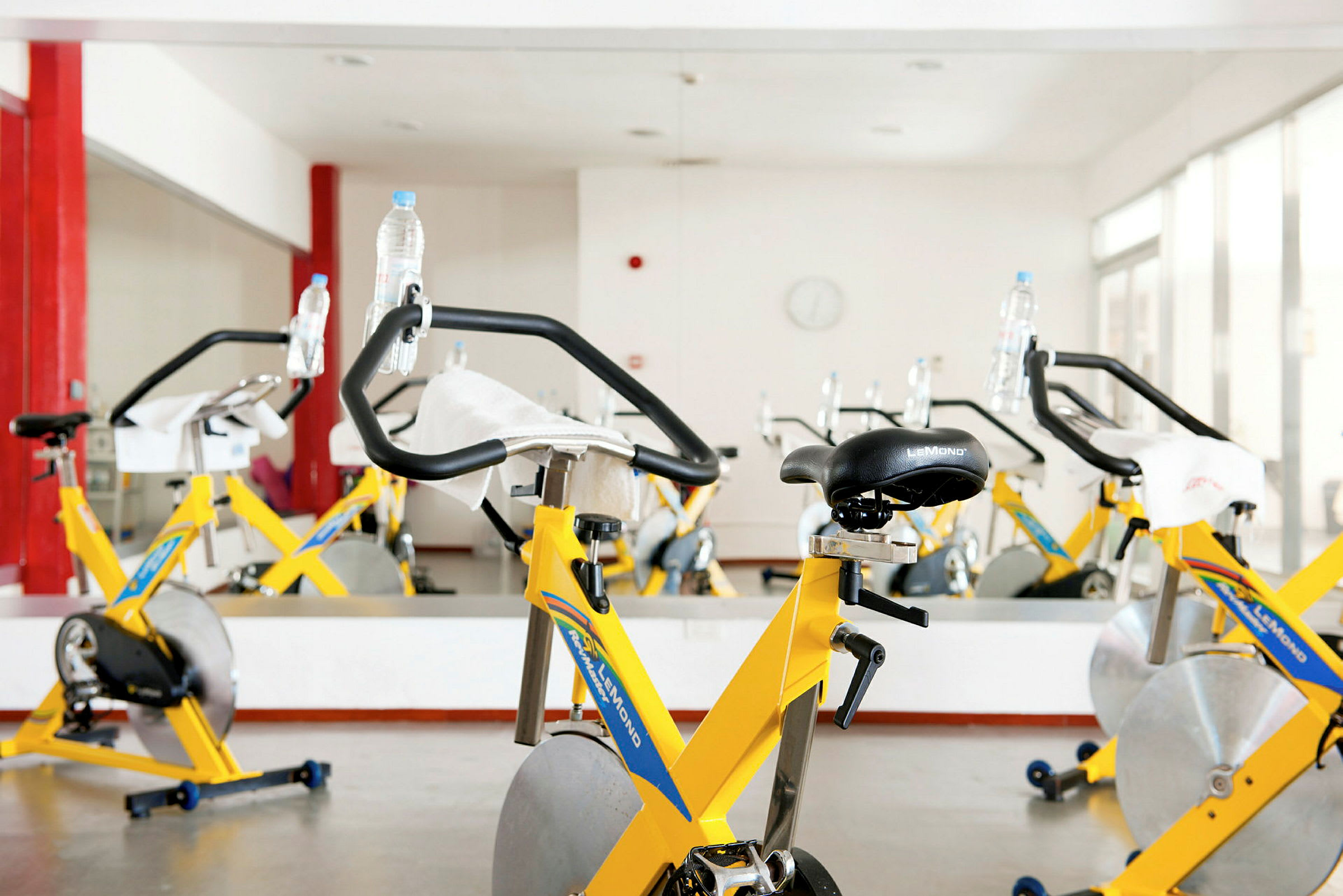 Interiør af et fitnesscenter med flere gule motionscykler arrangeret foran et spejl. (AI-genereret tekst)