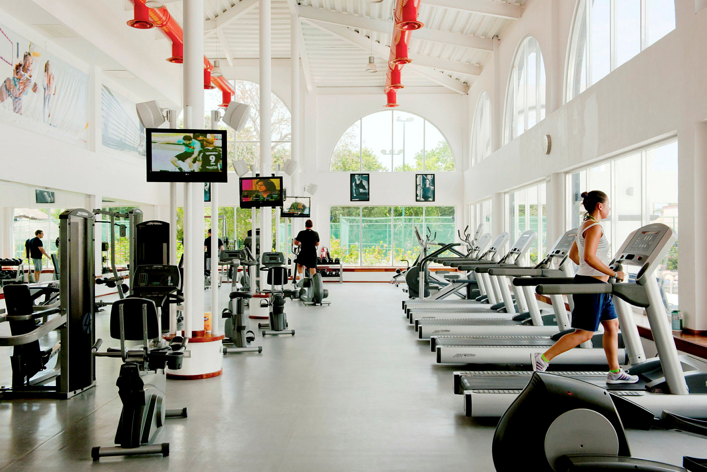 Et fitnesscenter med træningsmaskiner og løbebånd i et lyst lokale med store vinduer. (AI-genereret tekst)