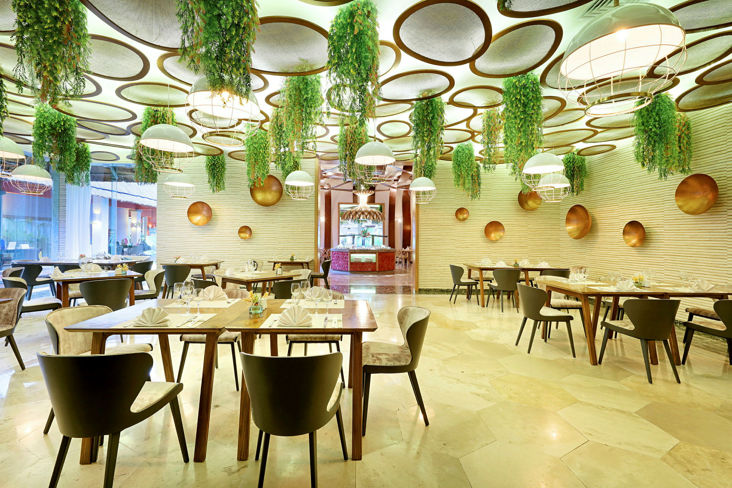 En restaurant med moderne indretning, hvor loftet er dekoreret med hængende grønne planter og runde paneler. Spisemøblerne er stilfulde, og bordene er dækket. (AI-genereret tekst)