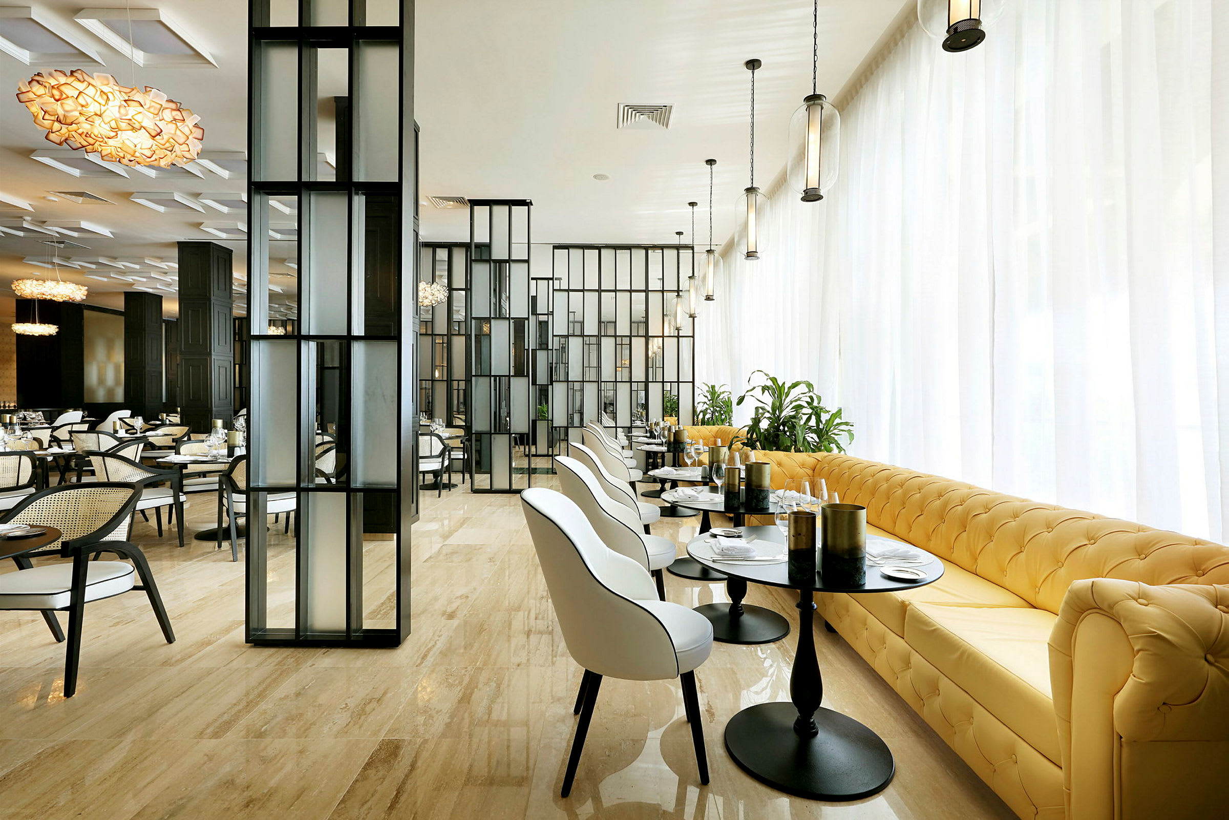 Et moderne spiseområde med elegant indretning, hvide stole, gule sofaer, glasborde og store glaspartier. (AI-genereret tekst)