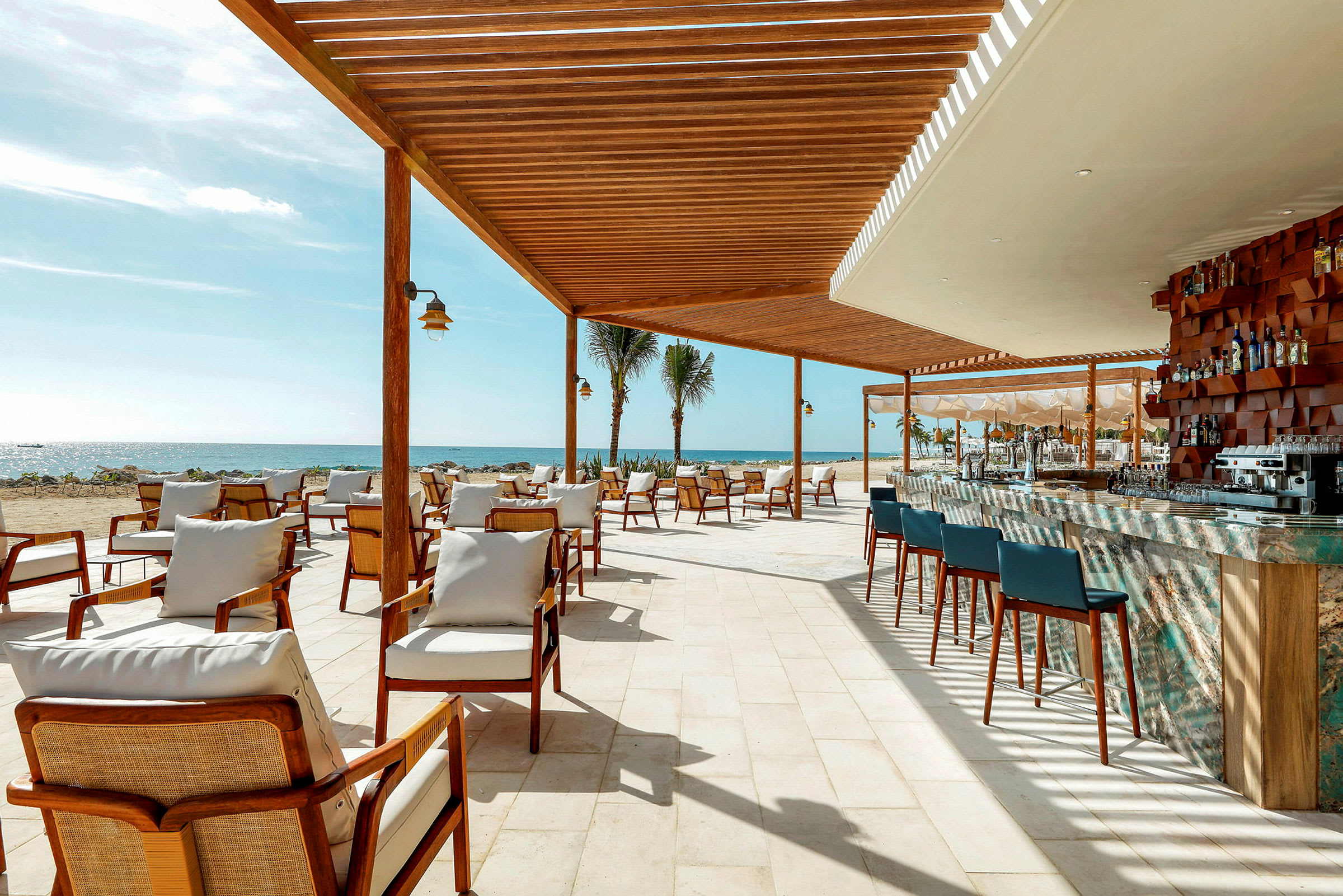 En udendørsrestaurant med siddepladser og en bar under en træpavillon ved stranden. (AI-genereret tekst)