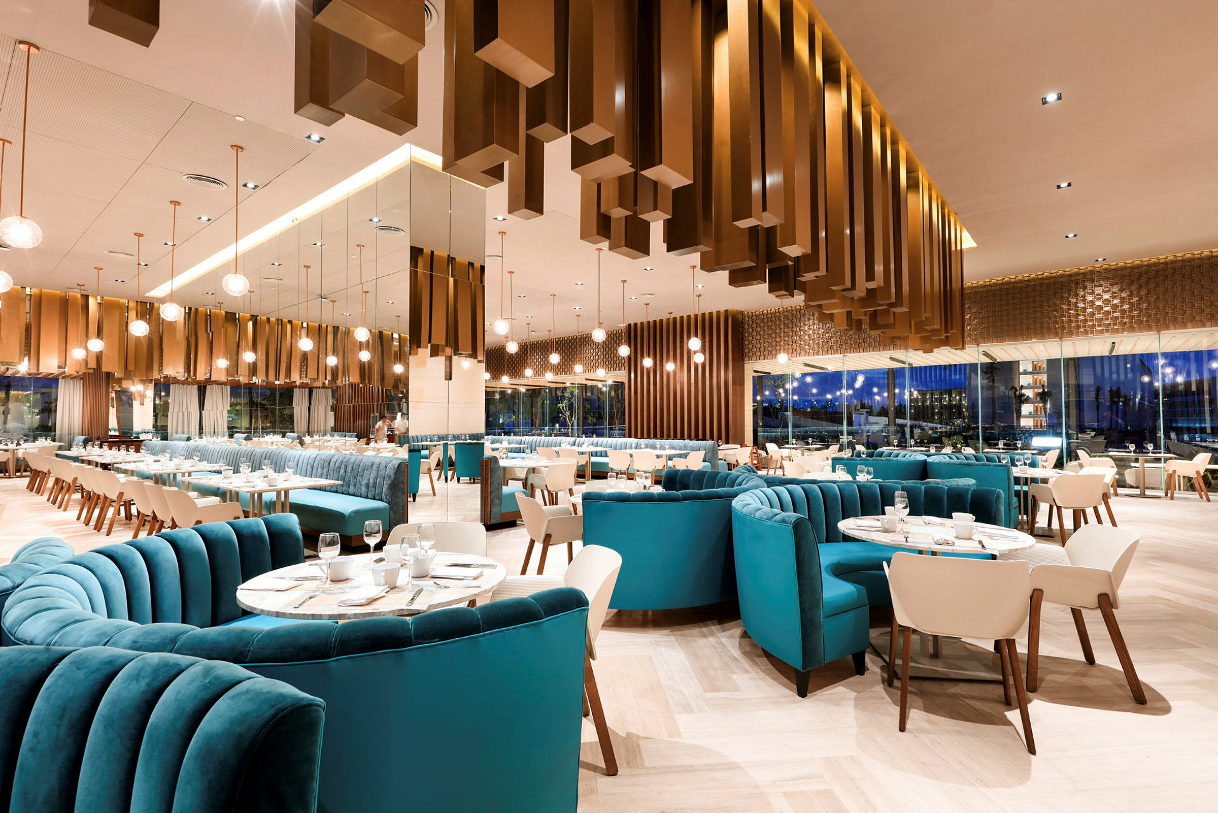 En moderne restaurant med elegante møbler, blå polstrede sofaer og hvide stole, samt tallerkener og vinglas placeret på bordene. (AI-genereret tekst)