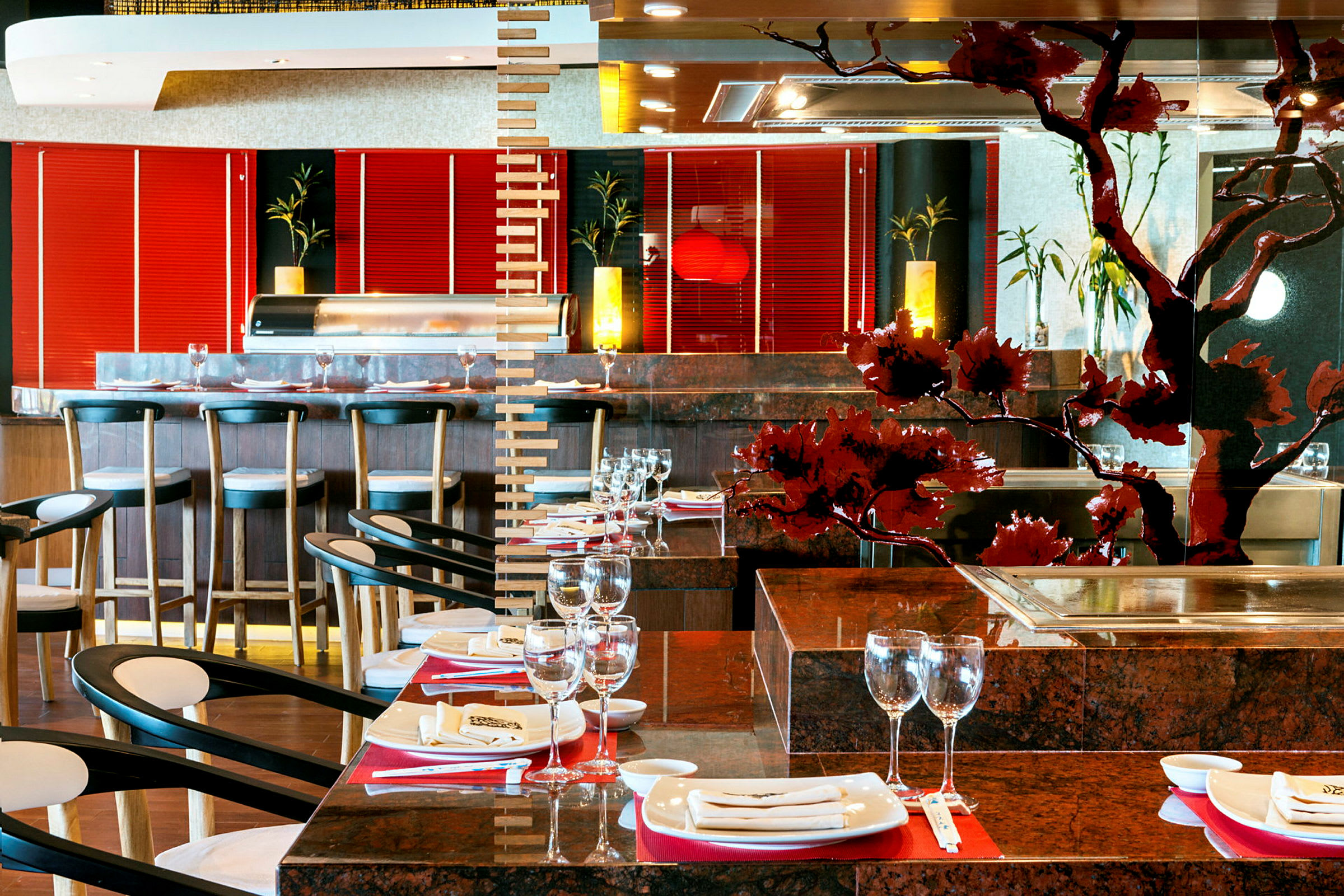 Et stilfuldt restaurantinteriør med borde dækket med glas og tallerkener samt stole. En bar med stole ses i baggrunden, og lokalet har dekorative detaljer og lysindslag. (AI-genereret tekst)