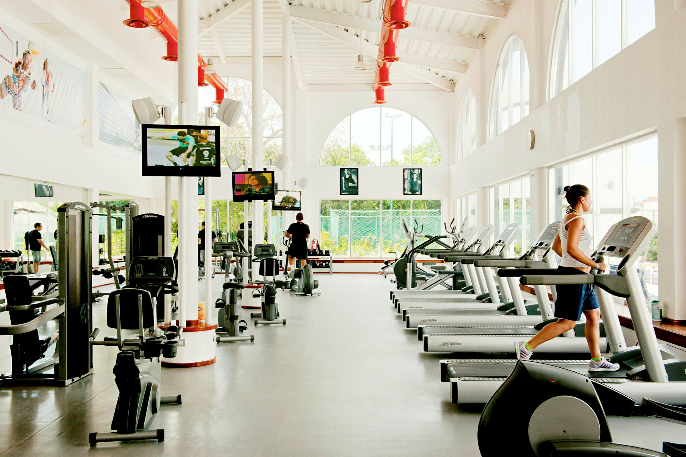 Et moderne fitnesscenter med træningsmaskiner, løbebånd og tv-skærme. (AI-genereret tekst)