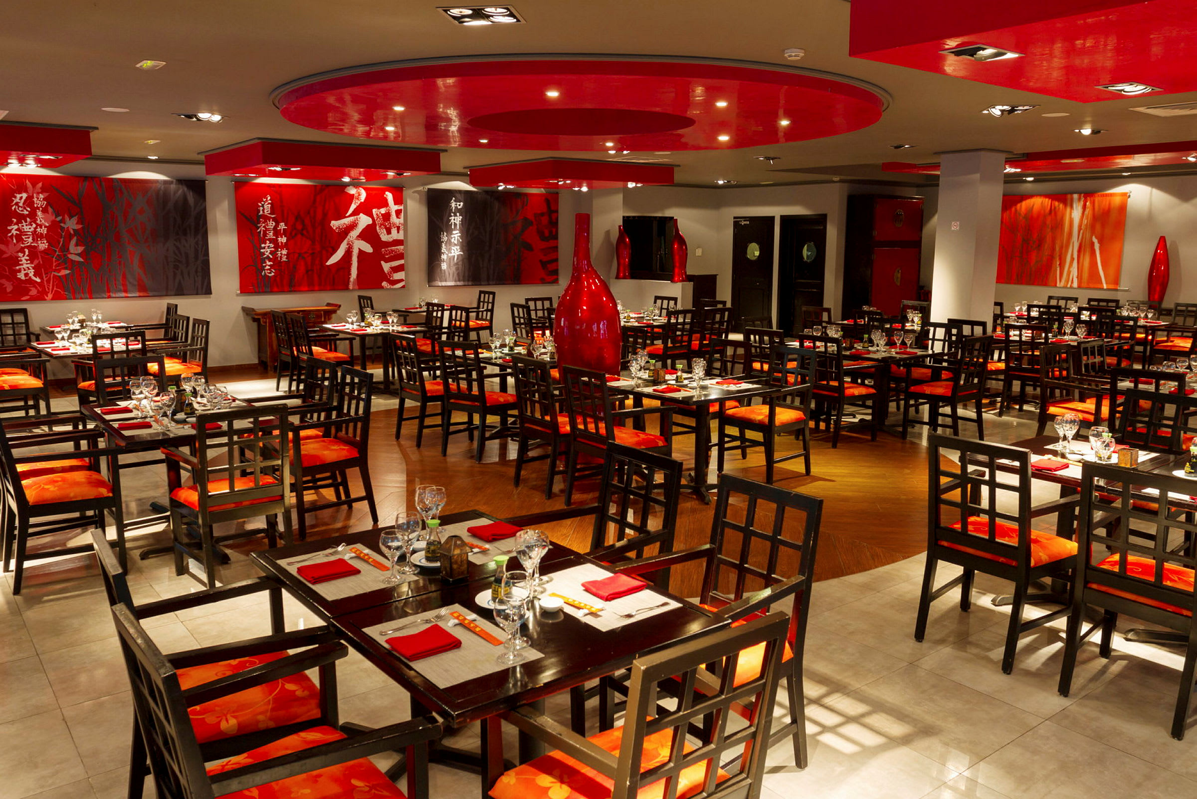 En restaurant med asiatisk indretning og sæt af borde og stole i træ. Væggene er dekoreret med kunst og røde accenter. (AI-genereret tekst)