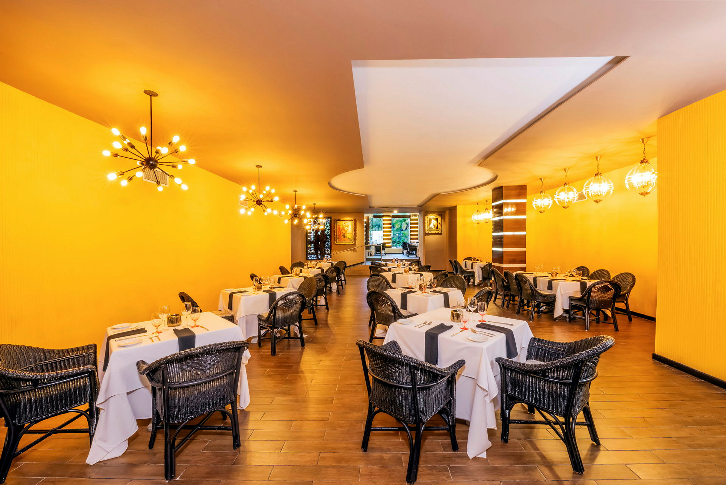 Restaurant med dækkede borde og fletstole, gul væg og dekorative lamper. (AI-genereret tekst)