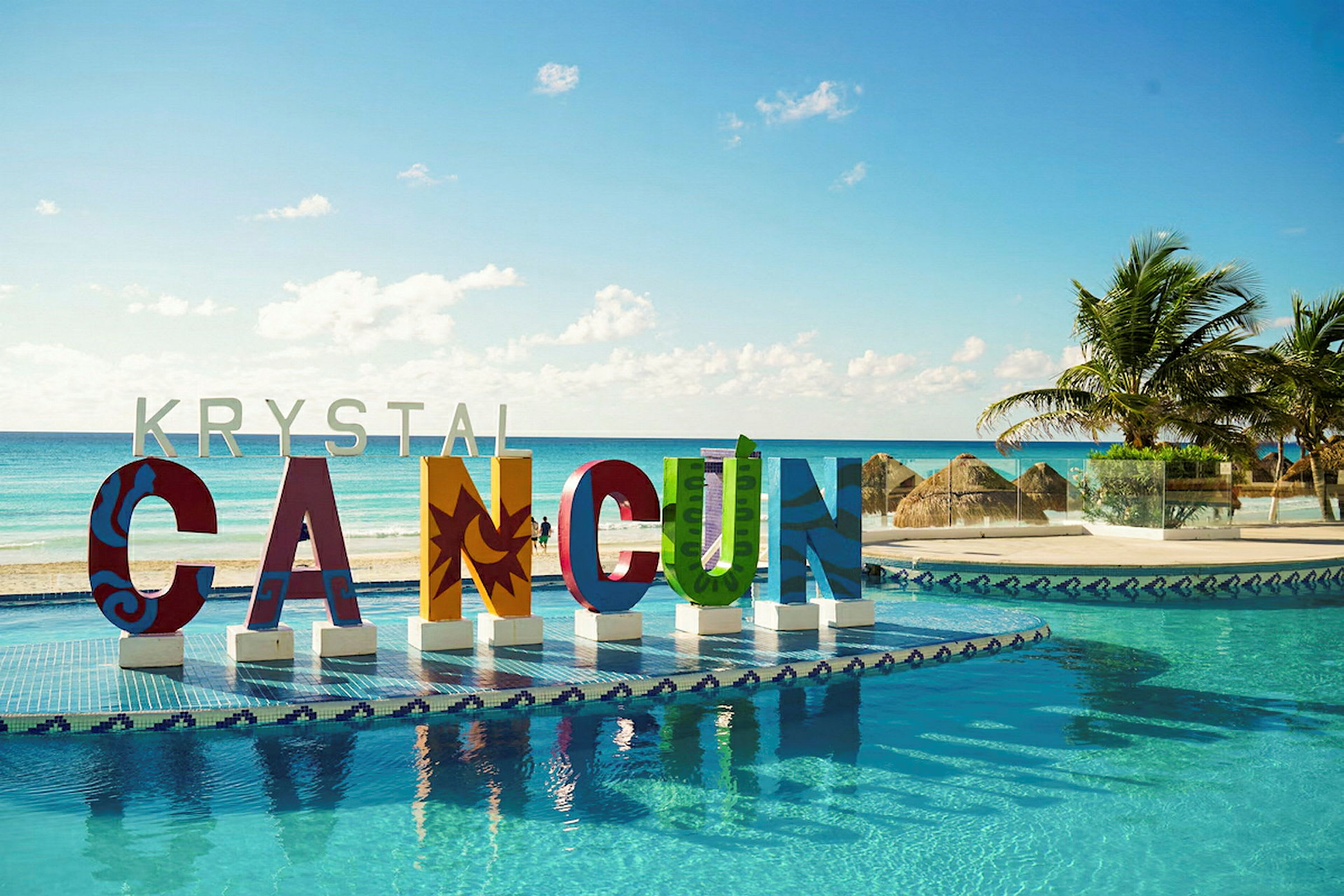 Farverige bogstaver, der danner ordet 'CANCUN' ved en pool med havudsigt og palmer. (AI-genereret tekst)