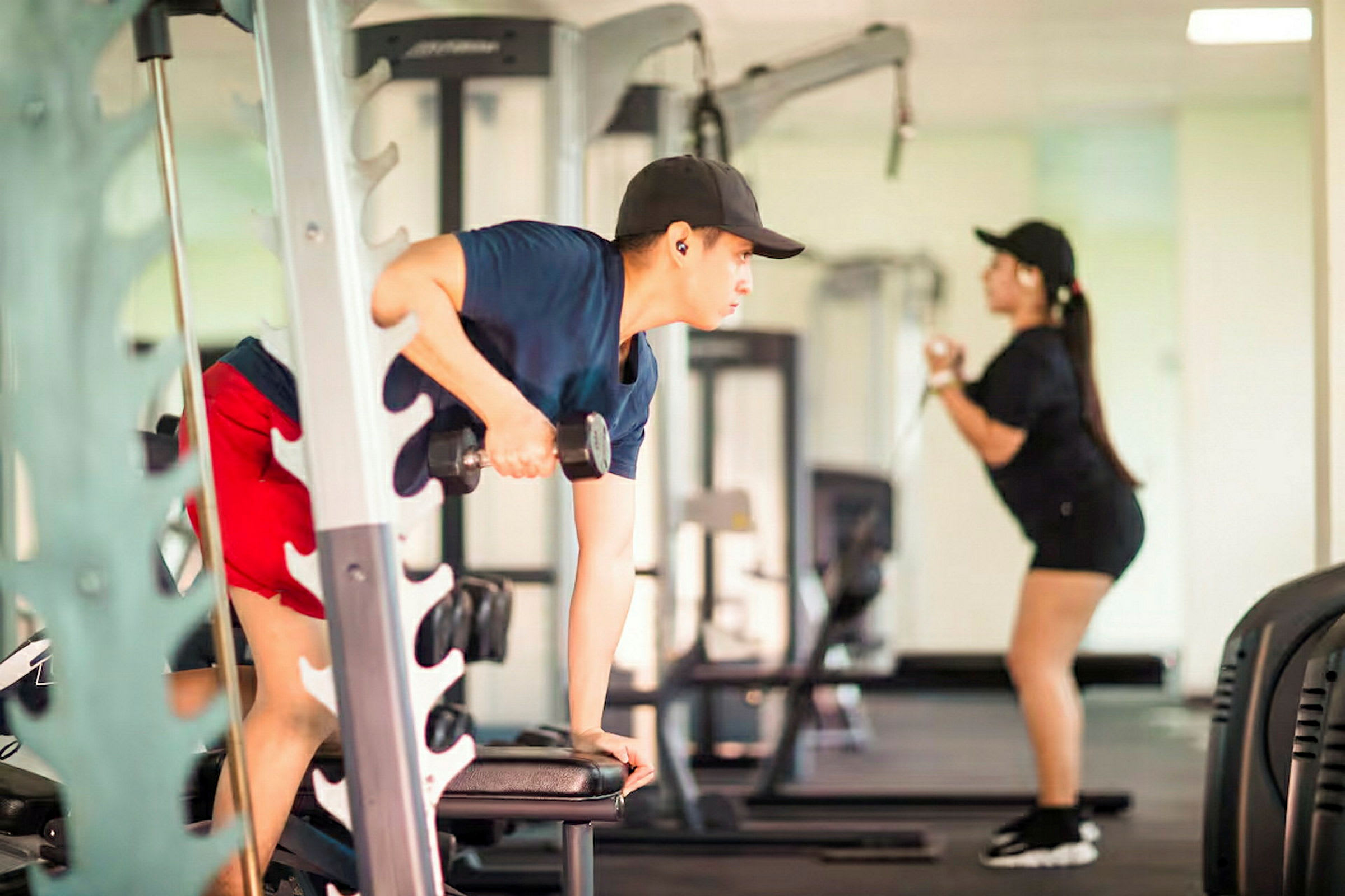 To personer træner i et fitnesscenter, hvor den ene bruger håndvægte, og den anden en kabelmaskine. (AI-genereret tekst)