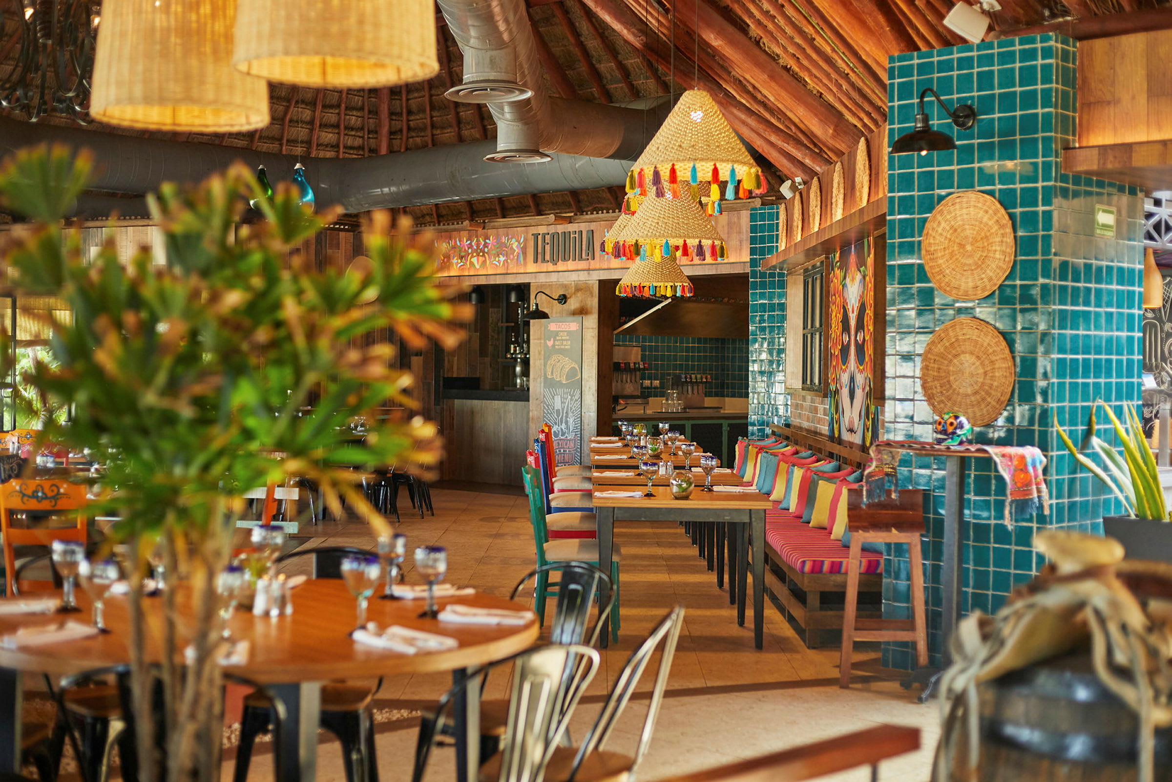 Et farverigt restaurantinteriør med borde og stole, dekorationerne inkluderer puder, grønne planter og hængende lamper. (AI-genereret tekst)