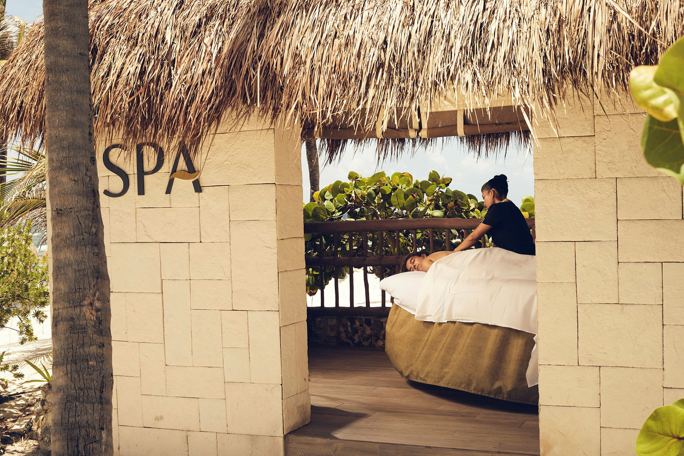 En udendørs spa-pavillon under et stråtag, hvor en person får en afslappende massage. (AI-genereret tekst)