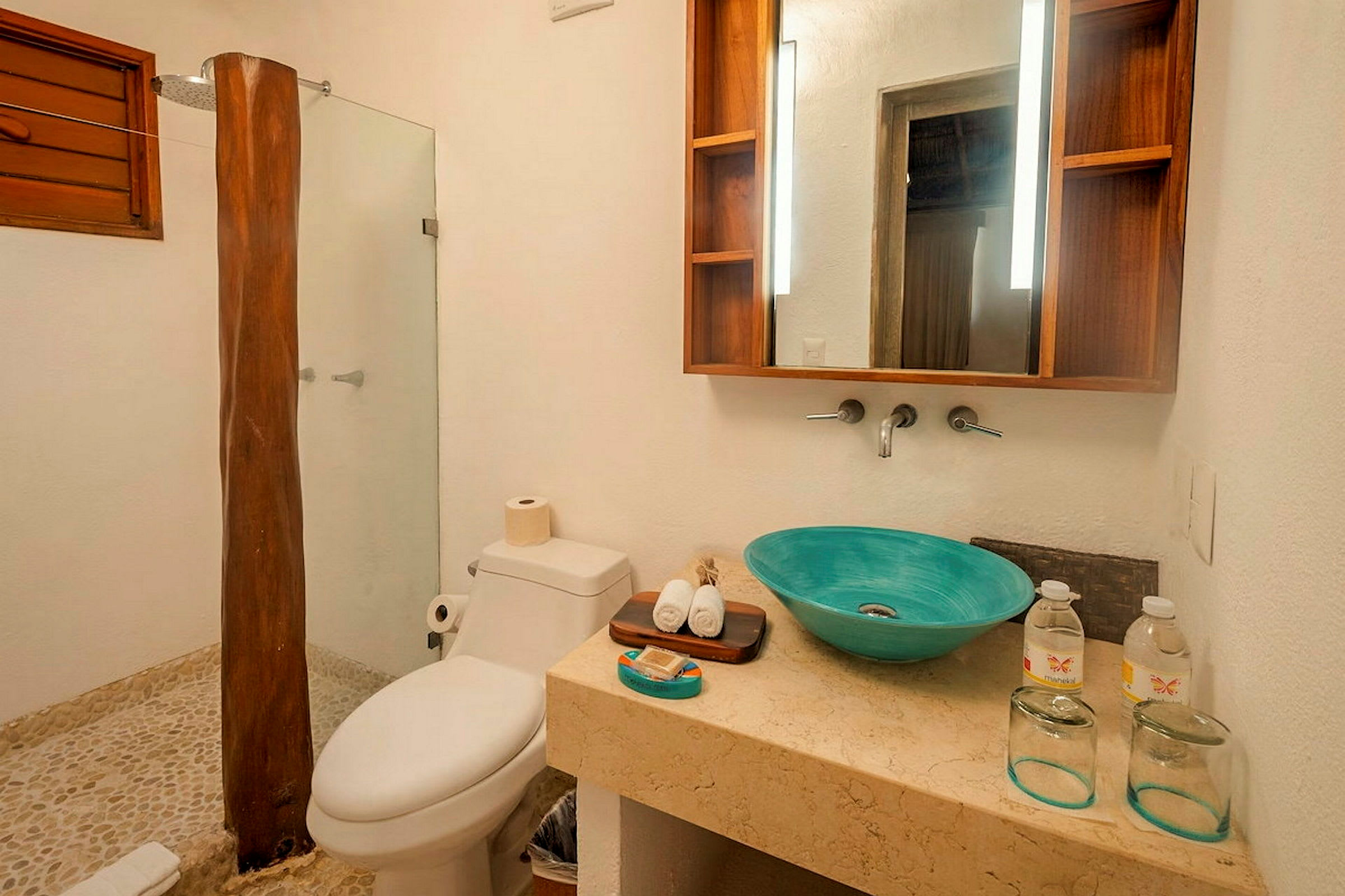 Billede af et badeværelse med brusehjørne, toilet og håndvask med en turkis skål. Der er et spejl med trædetaljer og nogle toiletartikler på bordet. (AI-genereret tekst)