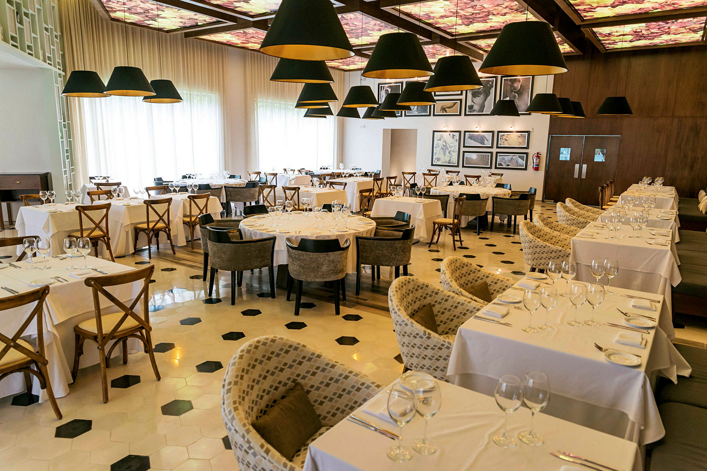 Billede af en elegant restaurant indrettet med hvide duge på bordene og komfortable stole, med dekorative lamper hængende fra loftet. (AI-genereret tekst)